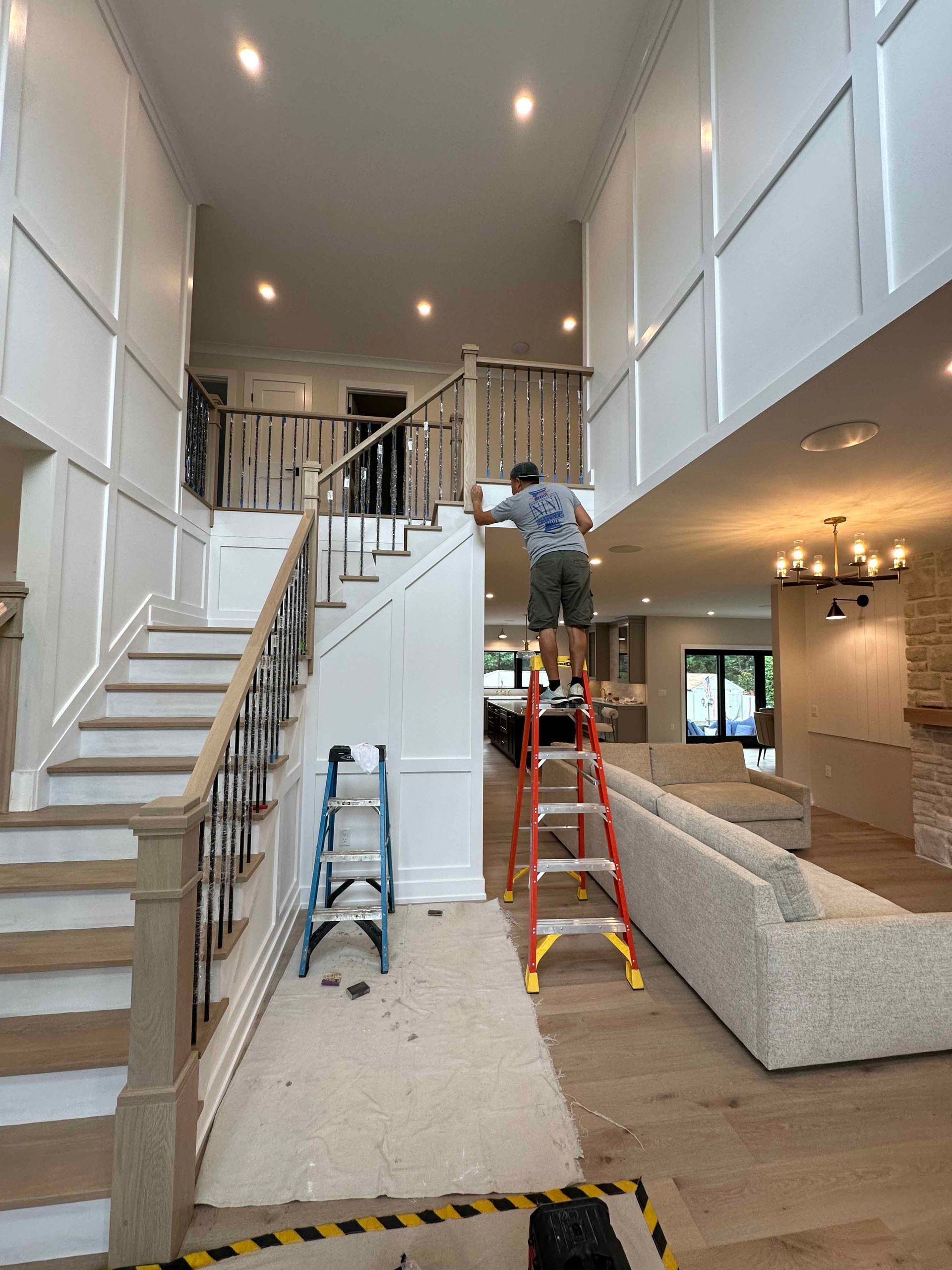 A man is standing on a ladder in a living room.
