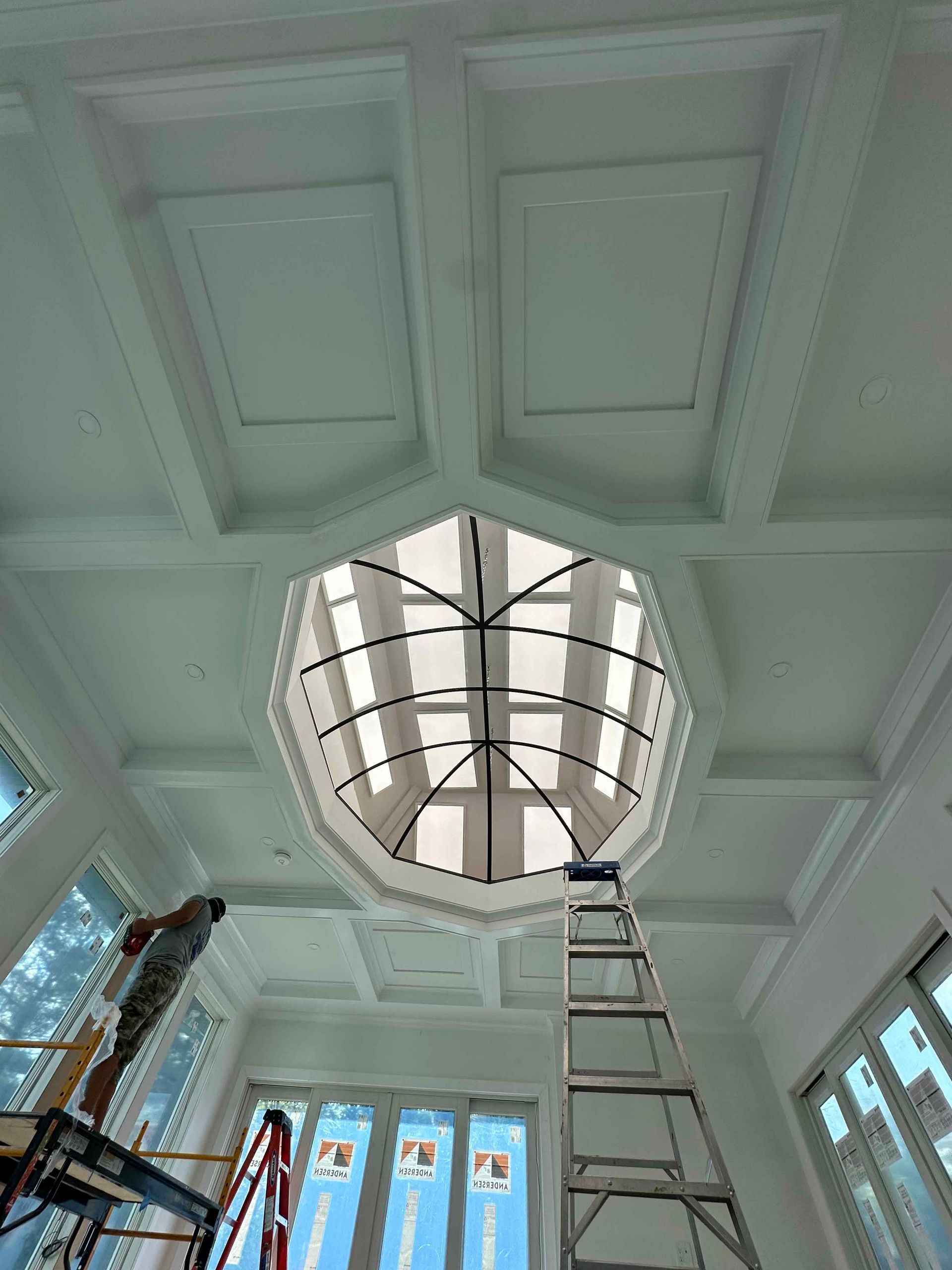 A man is standing on a ladder looking up at the ceiling of a building.