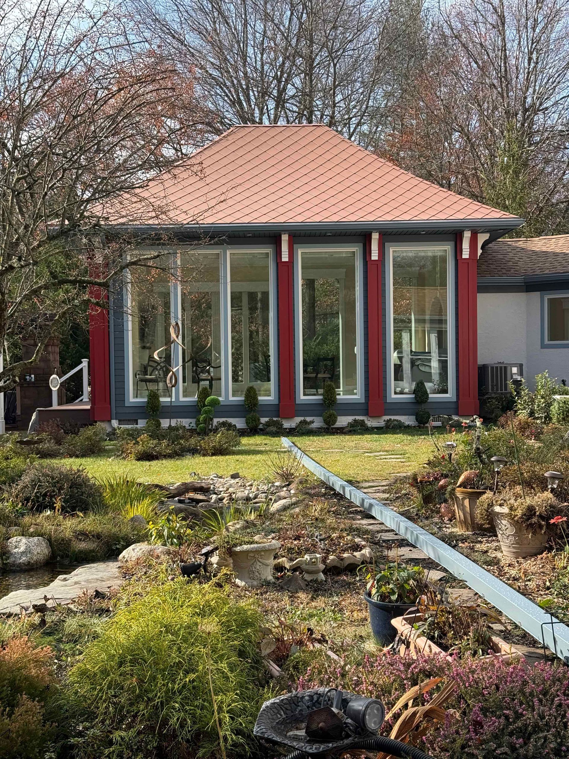 A house with a red roof and a lot of windows is surrounded by a garden.