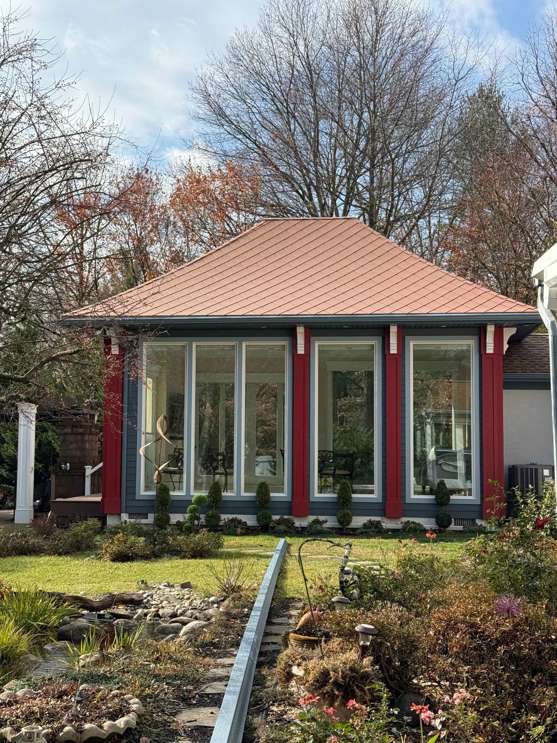 A small house with a red roof and a lot of windows is surrounded by trees.