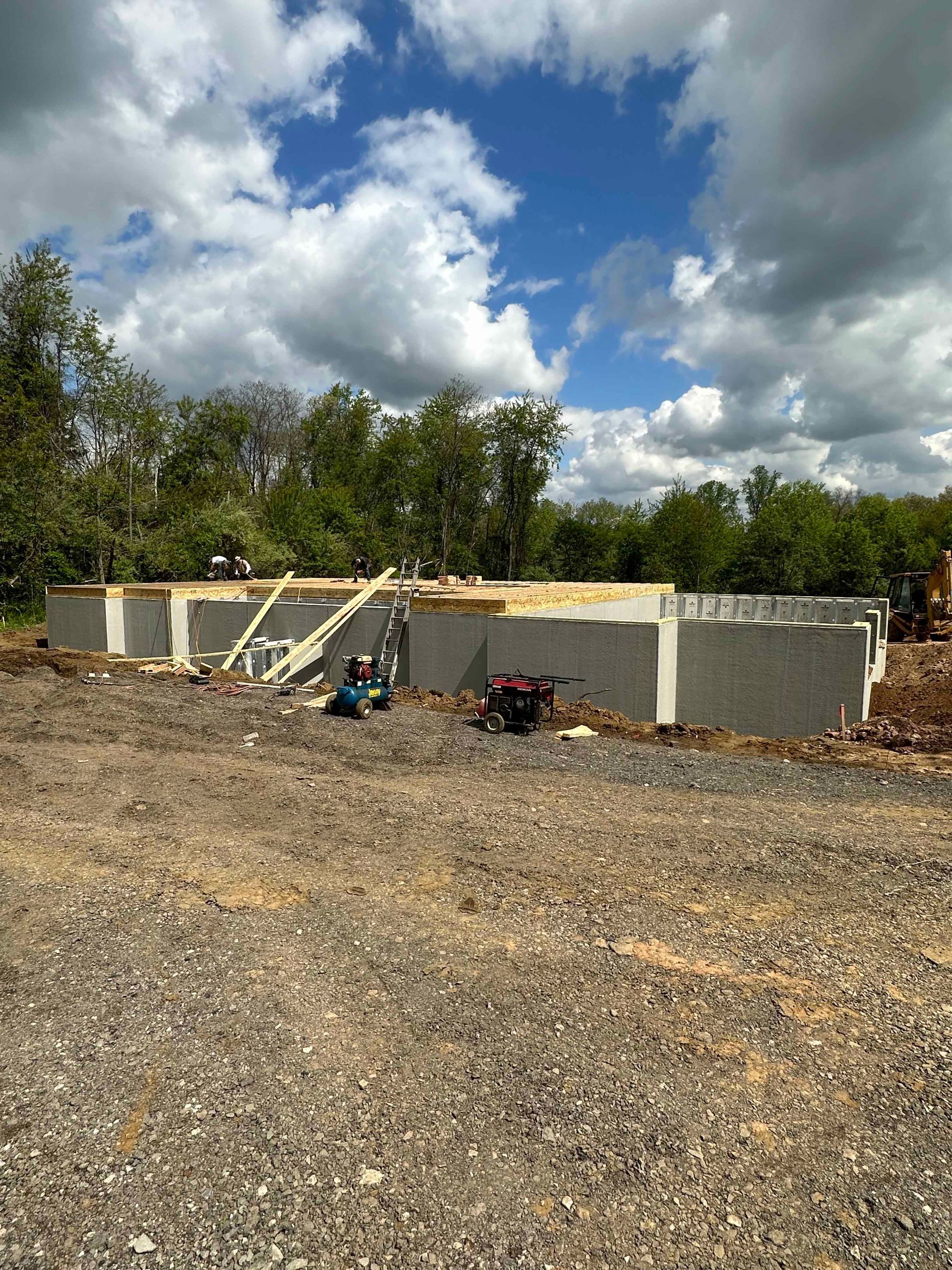 A large concrete wall is being built in a gravel lot.