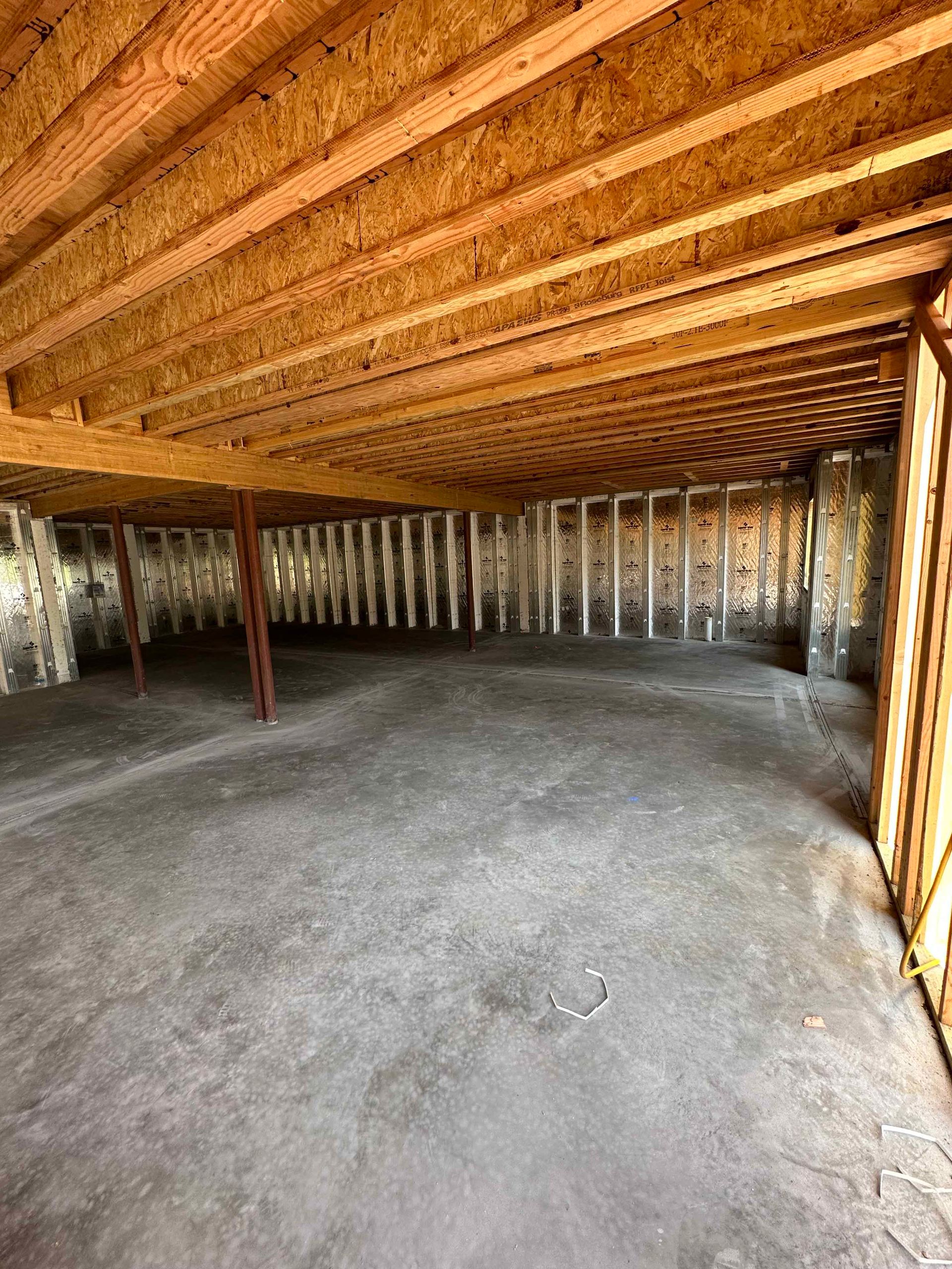 An empty basement with wooden beams and a concrete floor.