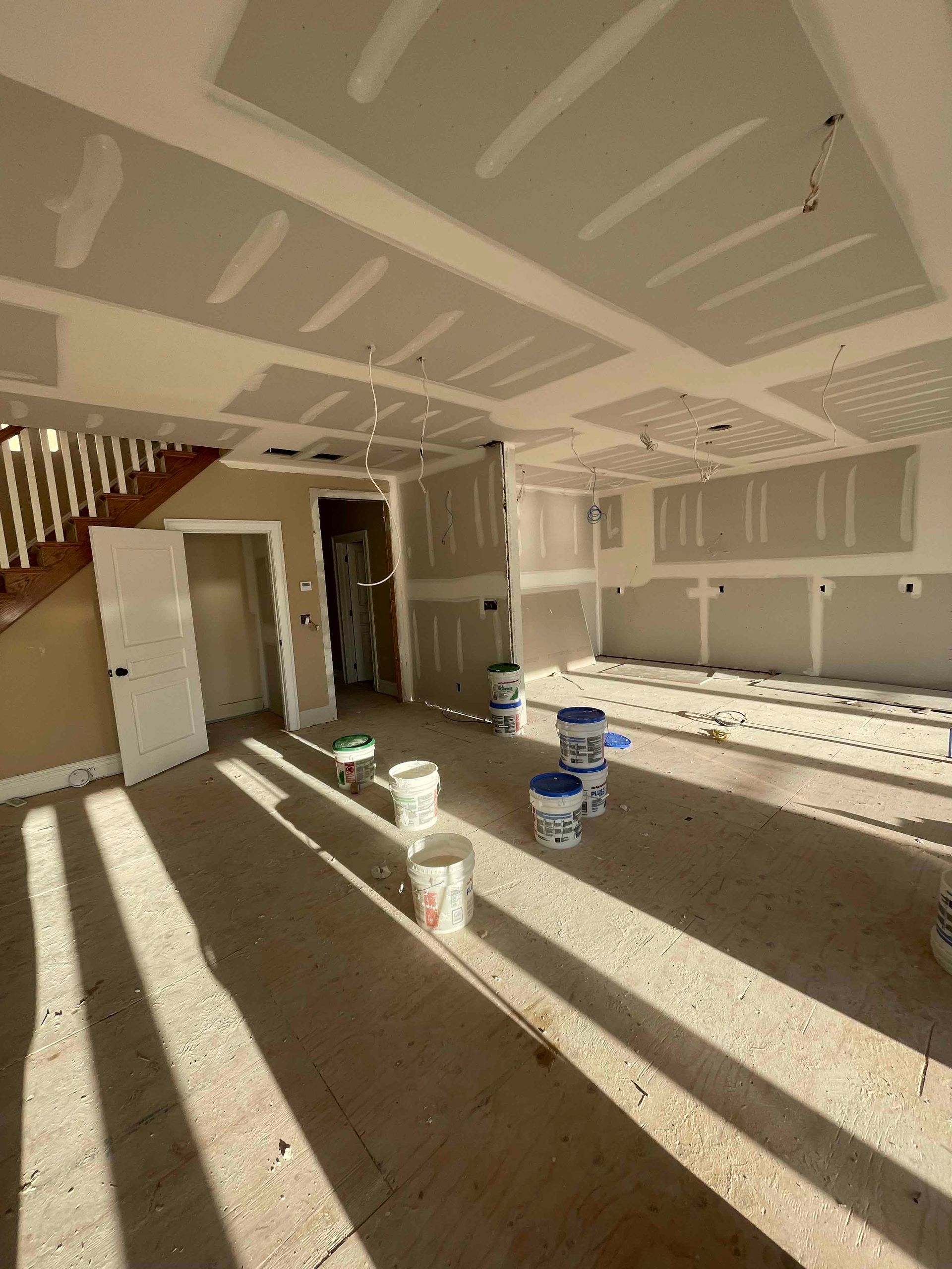 A room with buckets of paint on the floor and a staircase in the background.