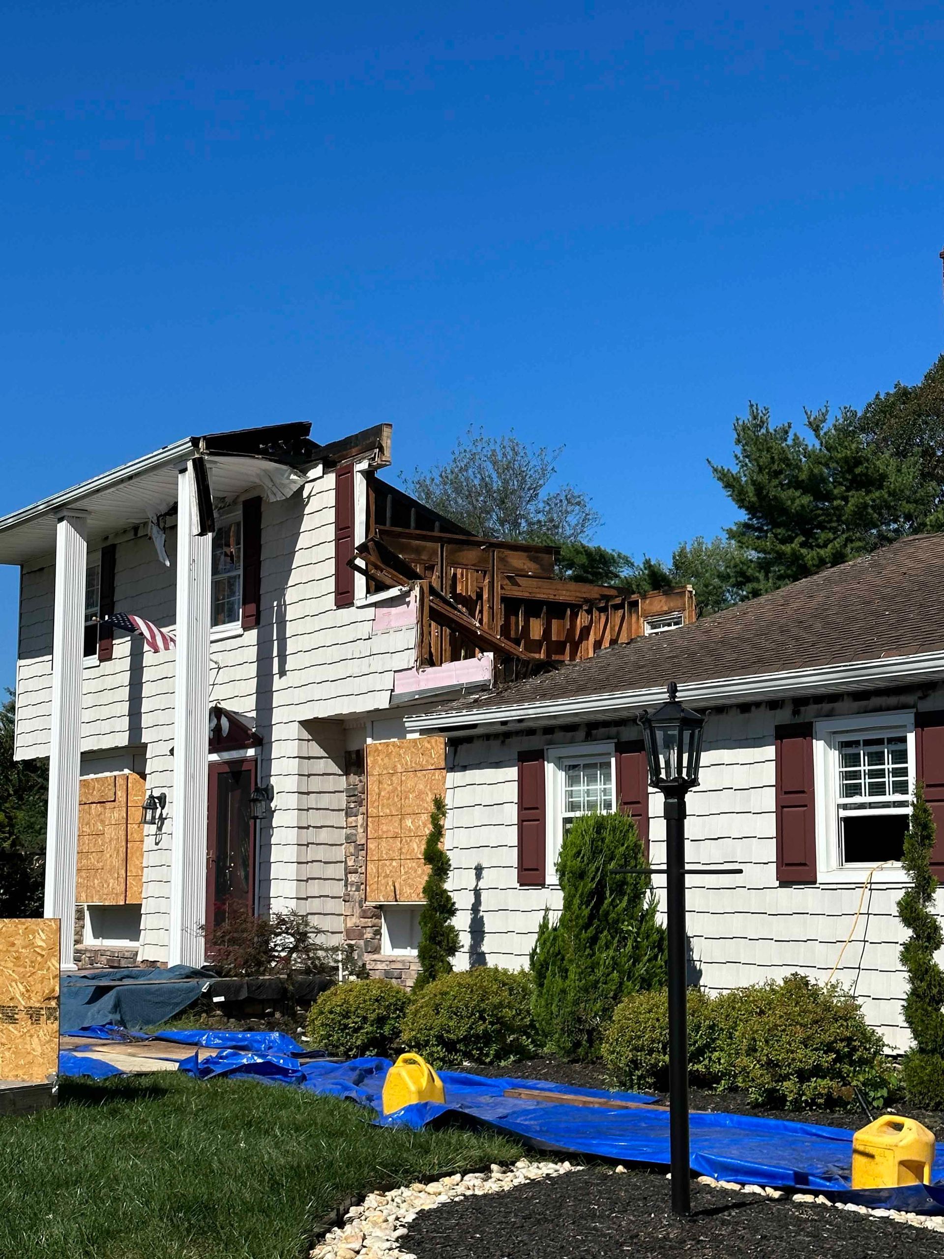 A white house with a roof that has been damaged by a fire.