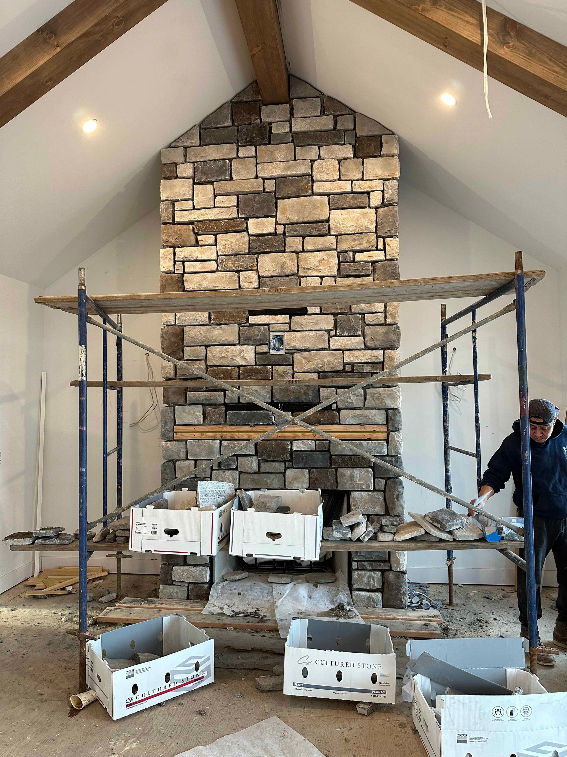 A man is standing in front of a large stone fireplace.