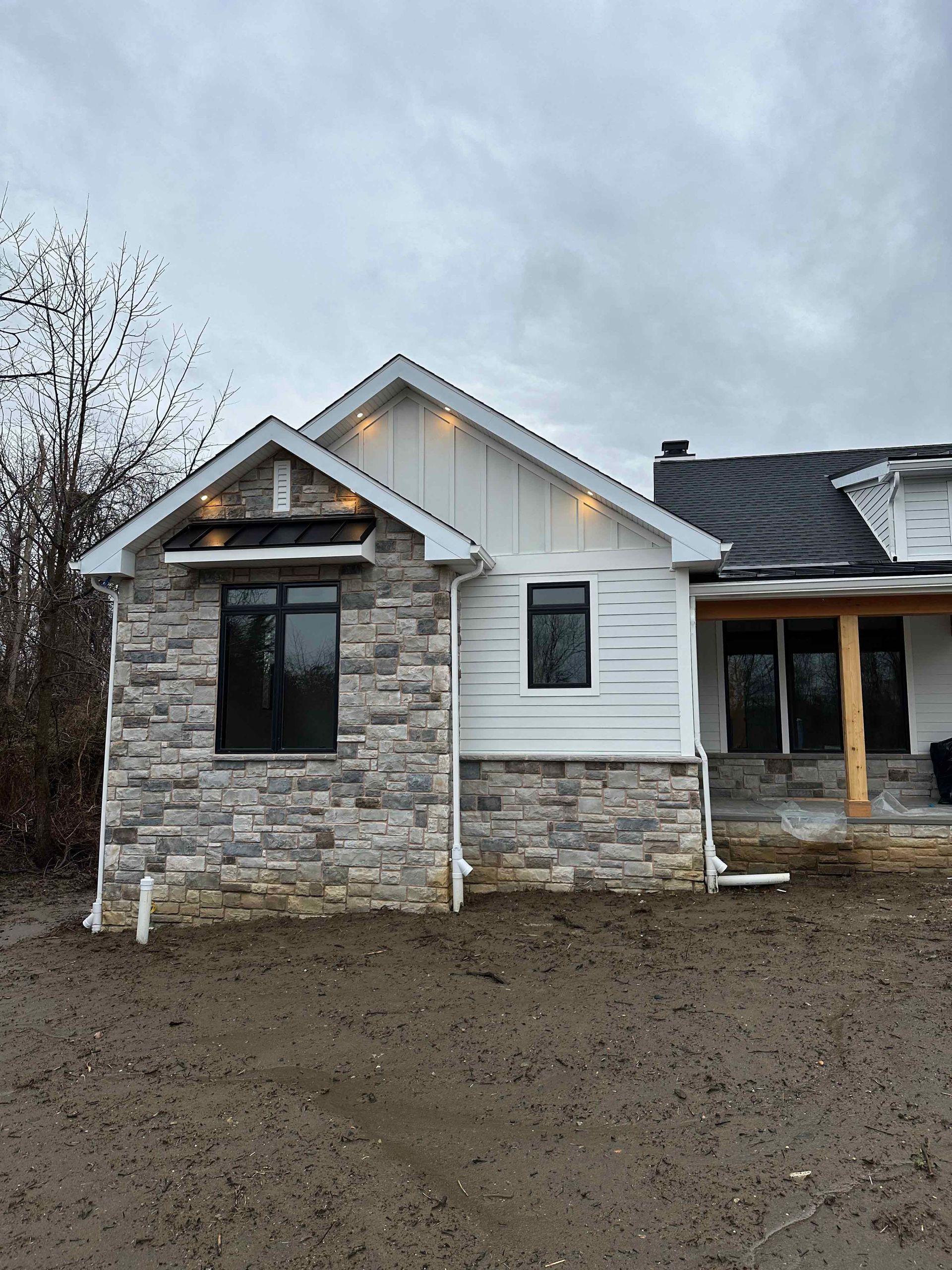A house with a stone facade and a white siding is sitting on top of a dirt field.