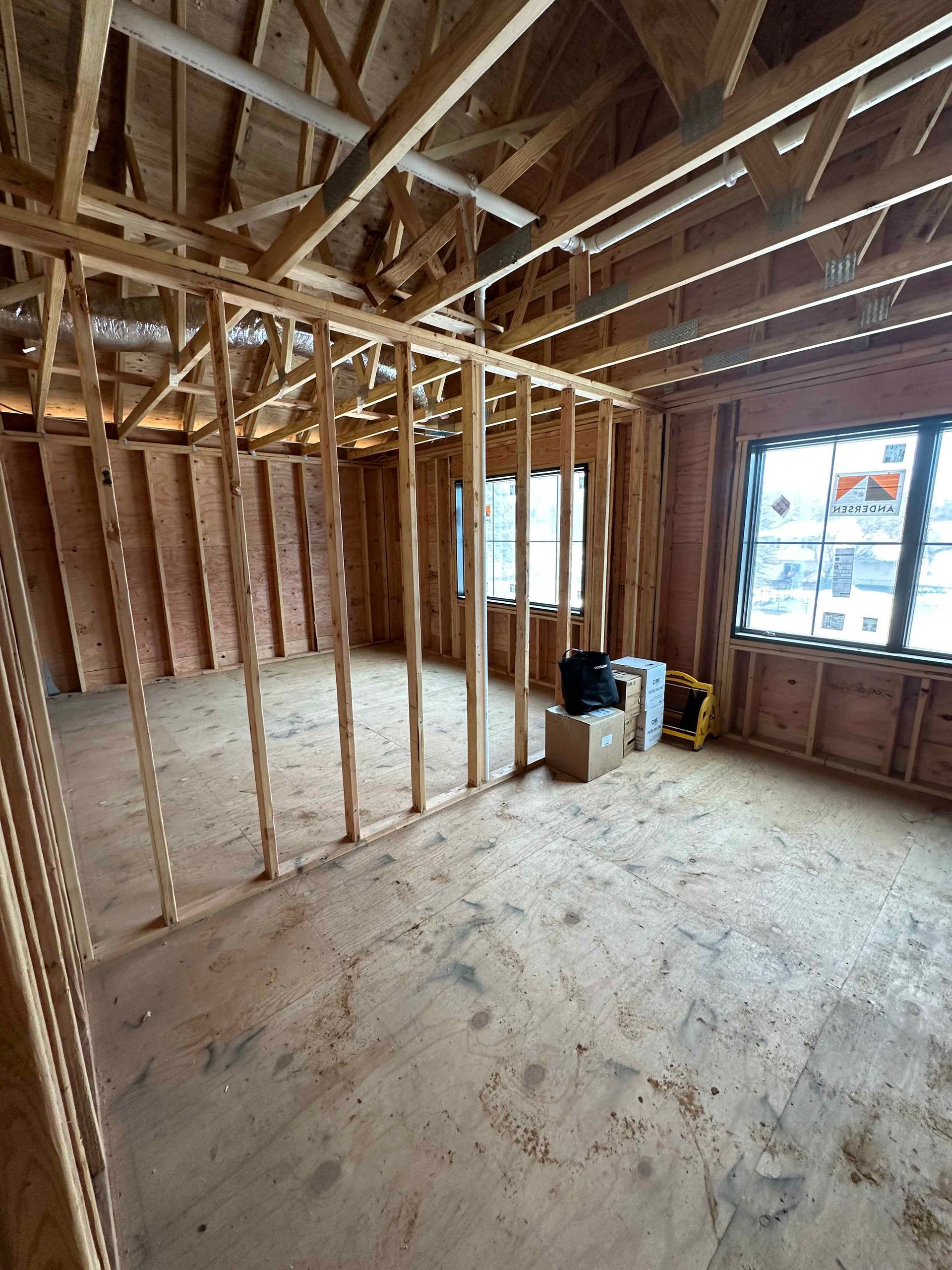 A room in a house under construction with wooden beams and windows.