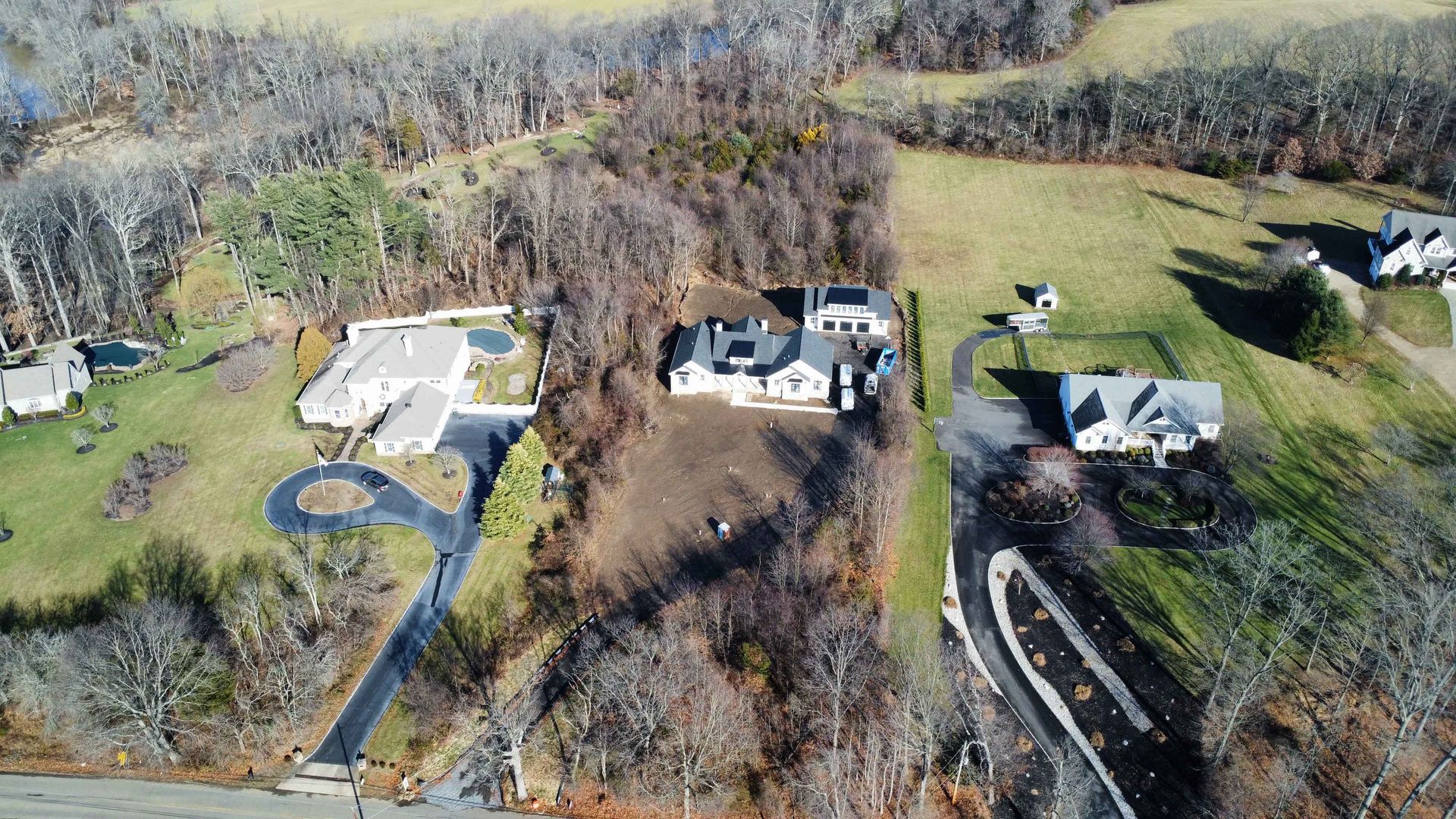 An aerial view of a large house in the middle of a lush green field surrounded by trees.