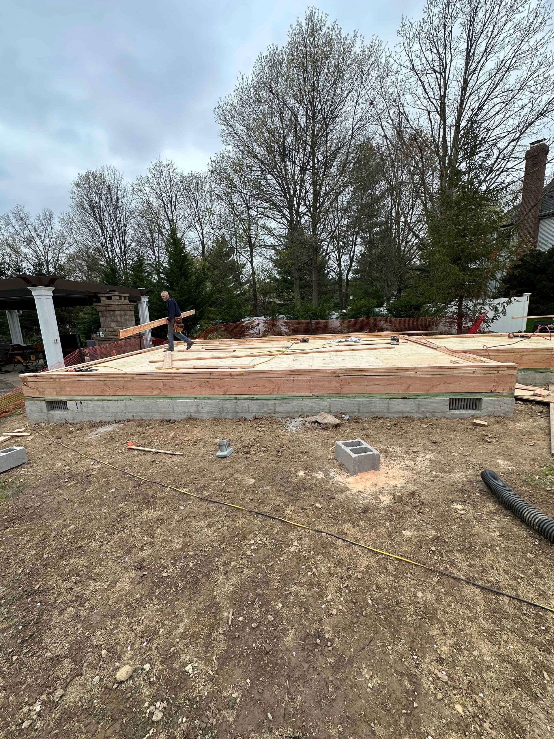 A man is standing on top of a pile of wood in a yard.