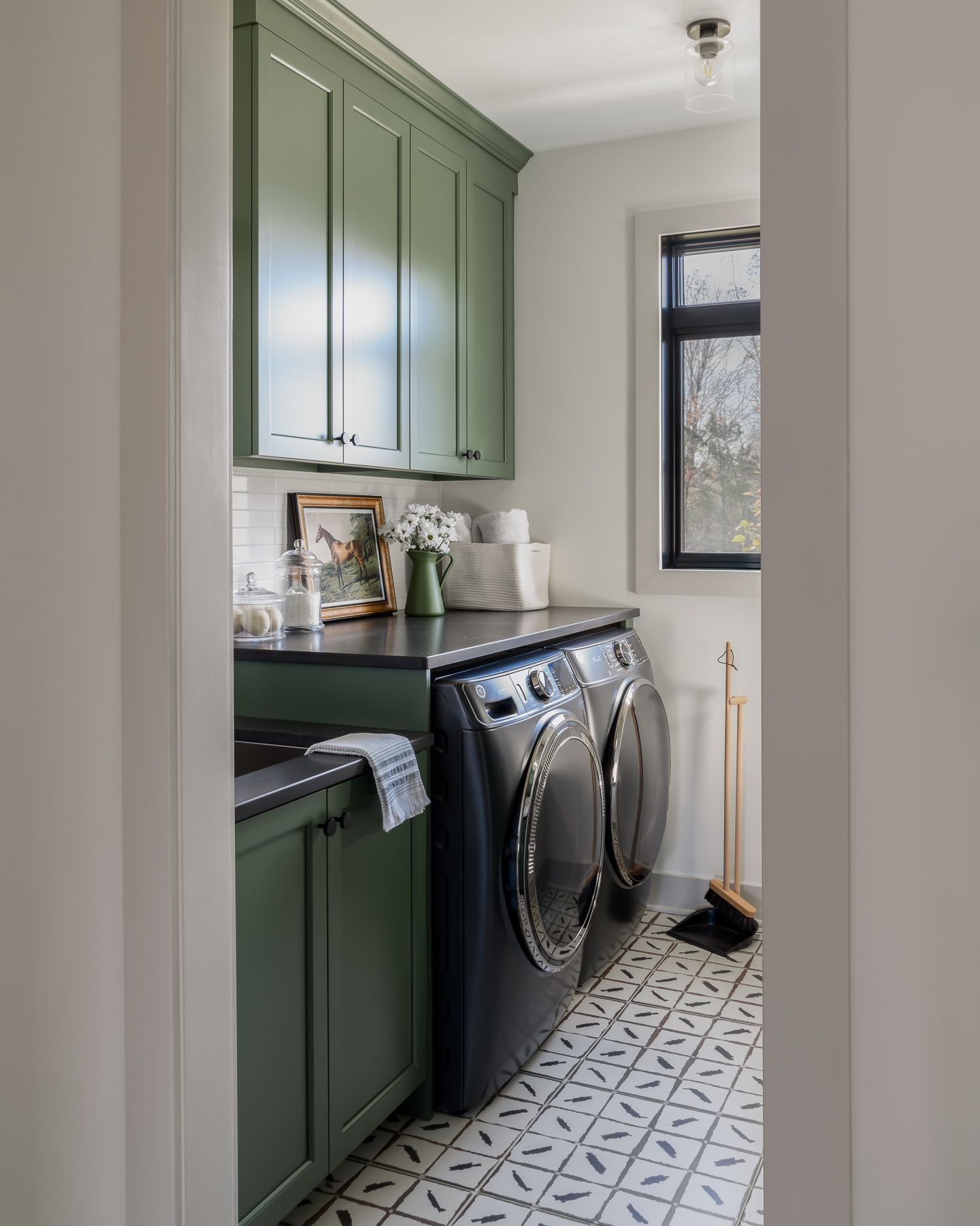 a laundry room with green cabinets, a dark washer and dryer, and patterned tile floor