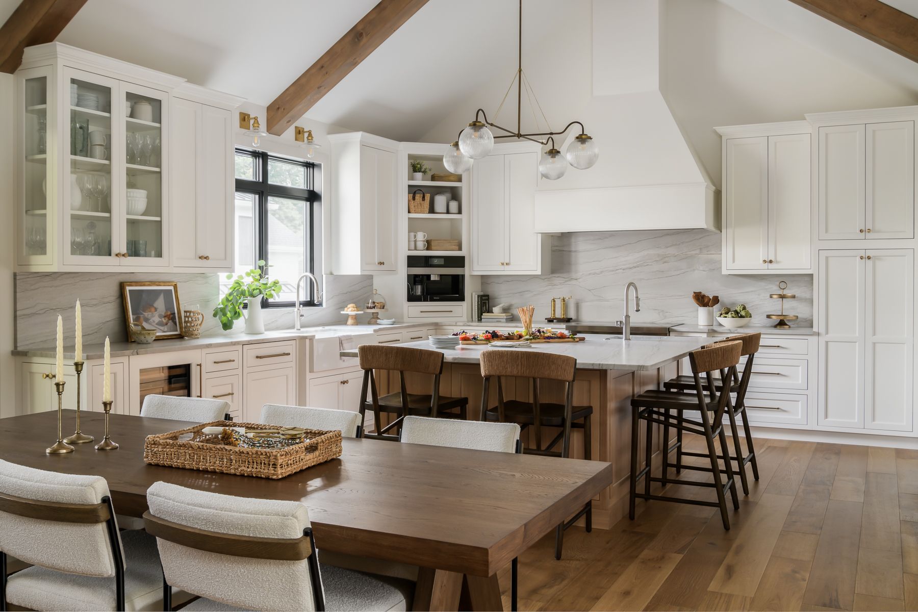 a spacious white kitchen with a large island, dining table, wood beams, and natural light