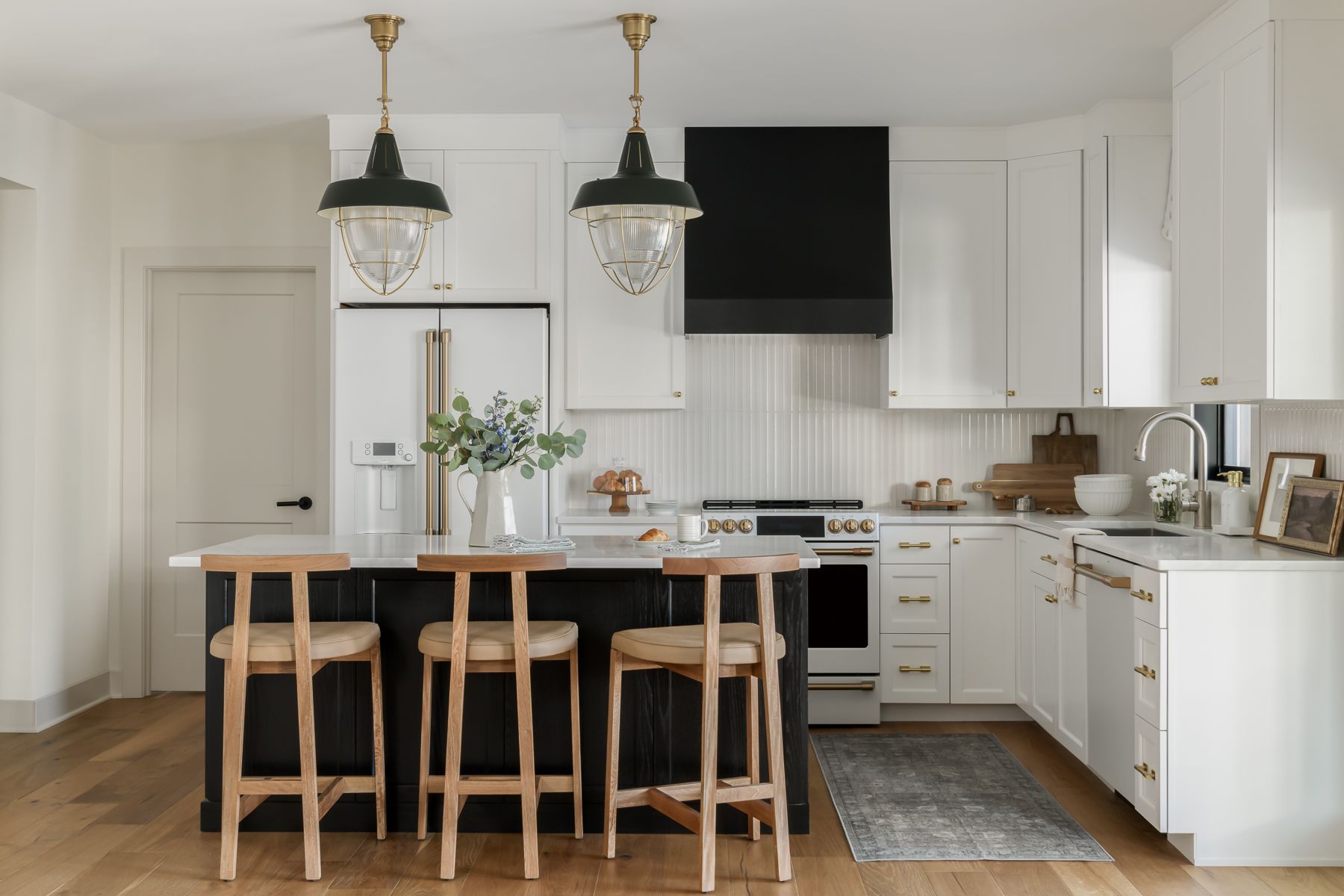 a bright kitchen featuring a black and white island with wooden stools, white cabinets, and two pendant lights