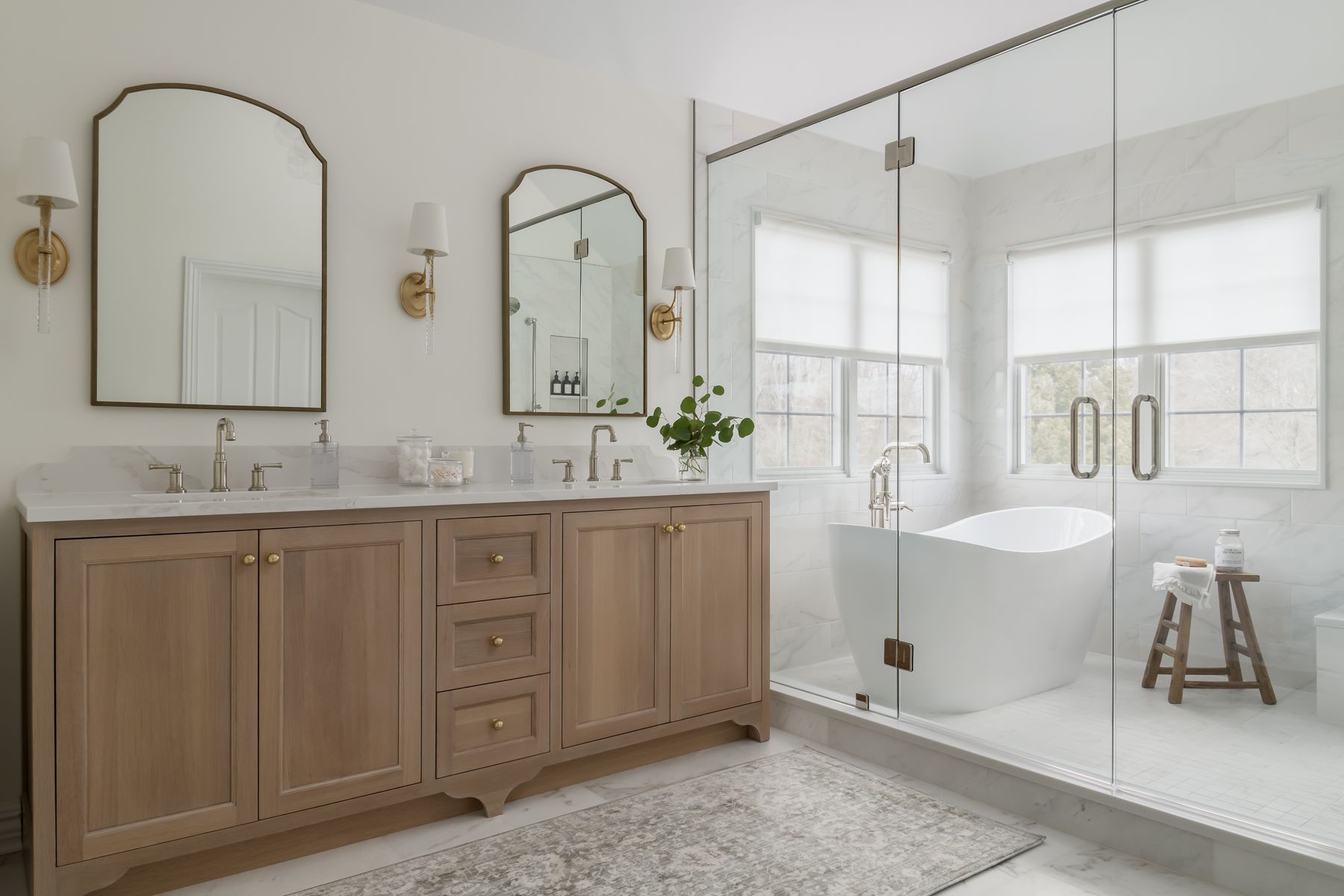 a bright, spacious bathroom with a wooden vanity, arched mirrors, a glass shower, and a freestanding tub