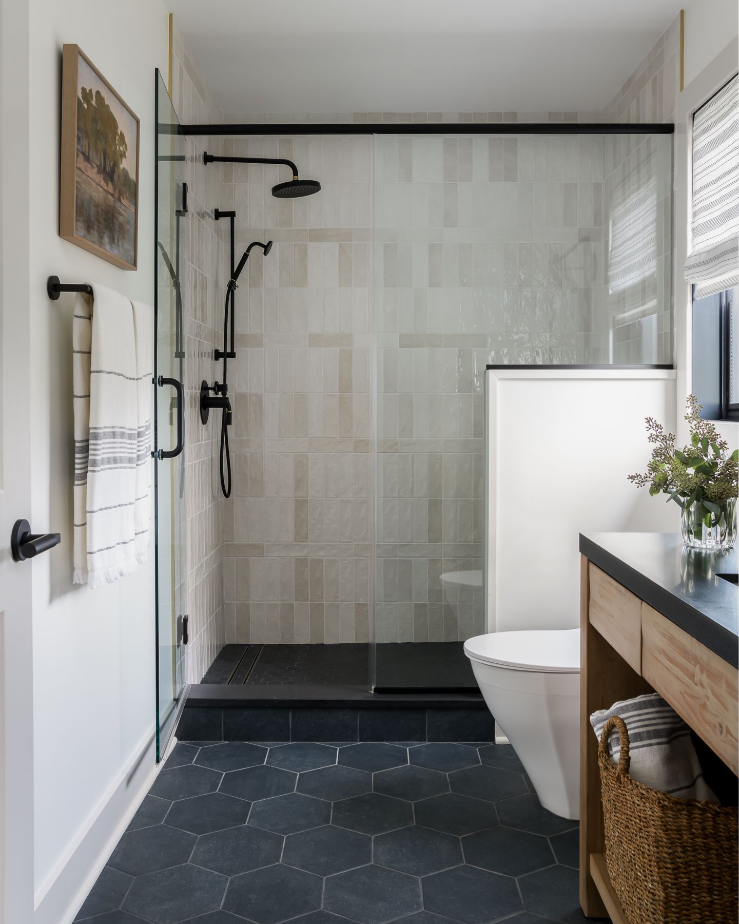 a modern bathroom with a glass shower, black hexagon tile floor, and a wooden vanity