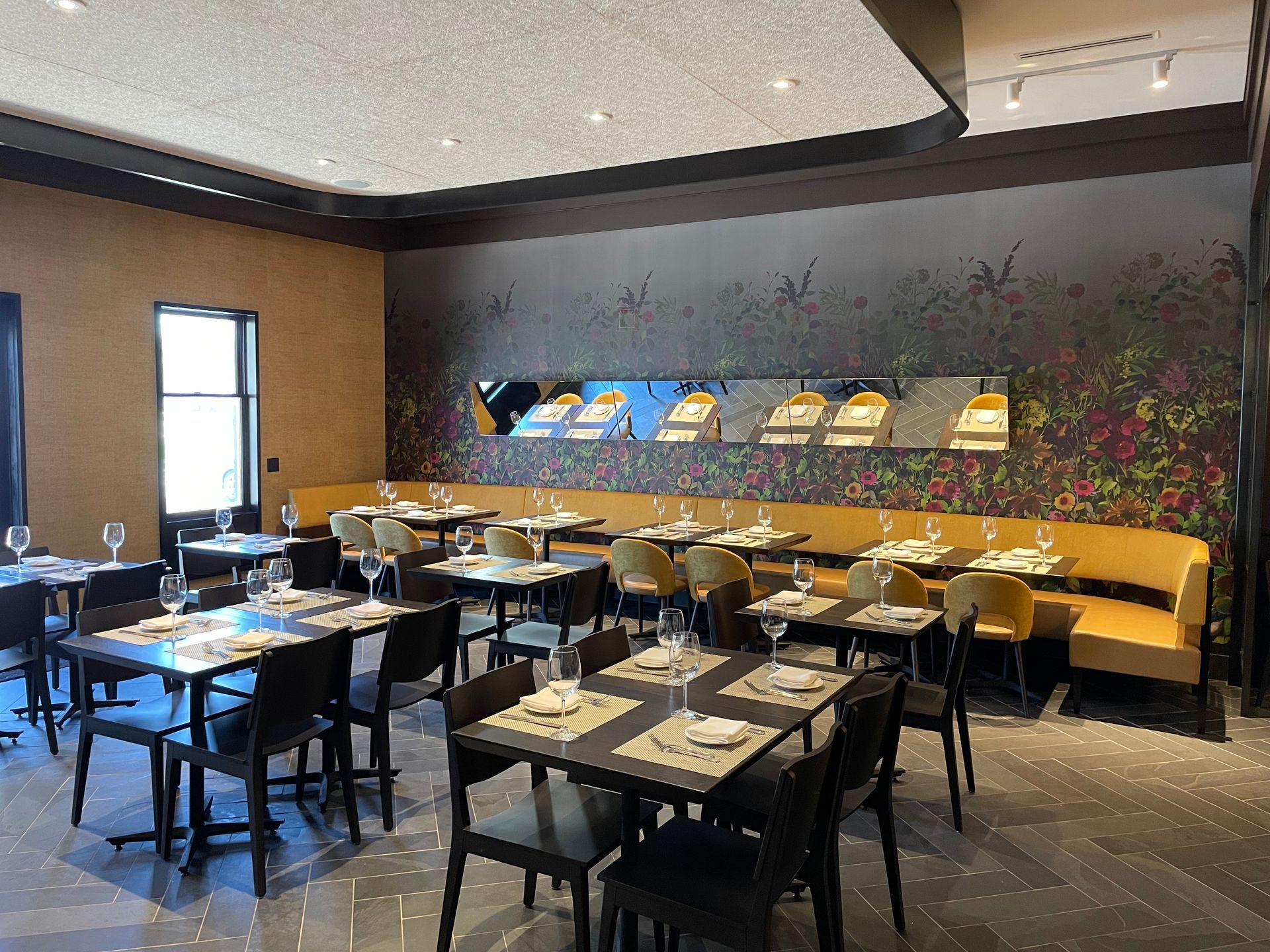 A large dining room with tables and chairs and a floral wall.