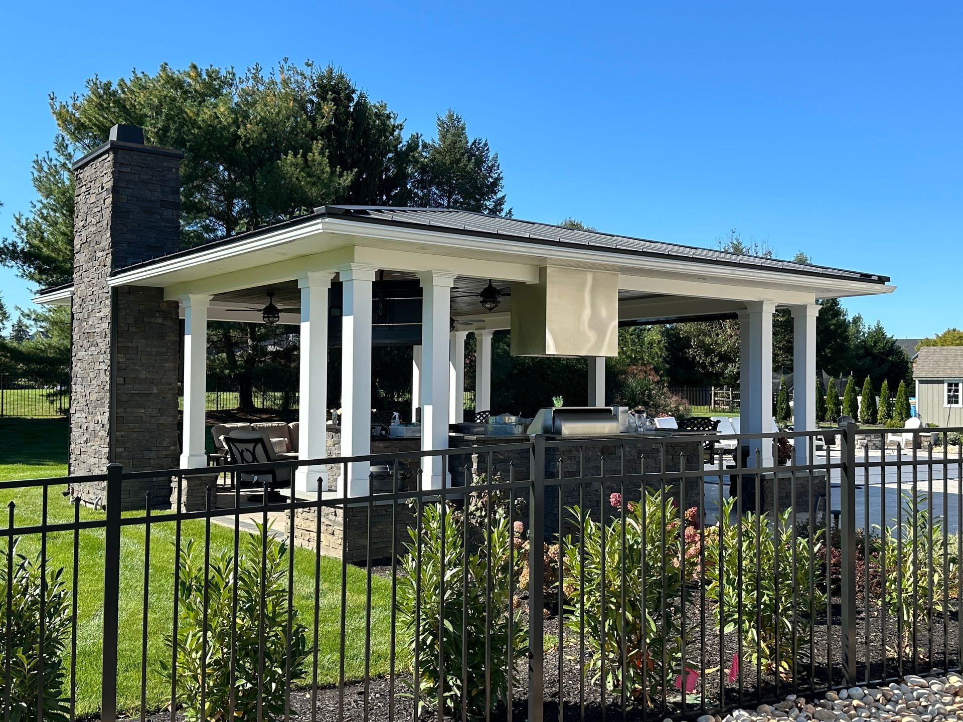 A pavilion with a grill and a fireplace is surrounded by a fence.