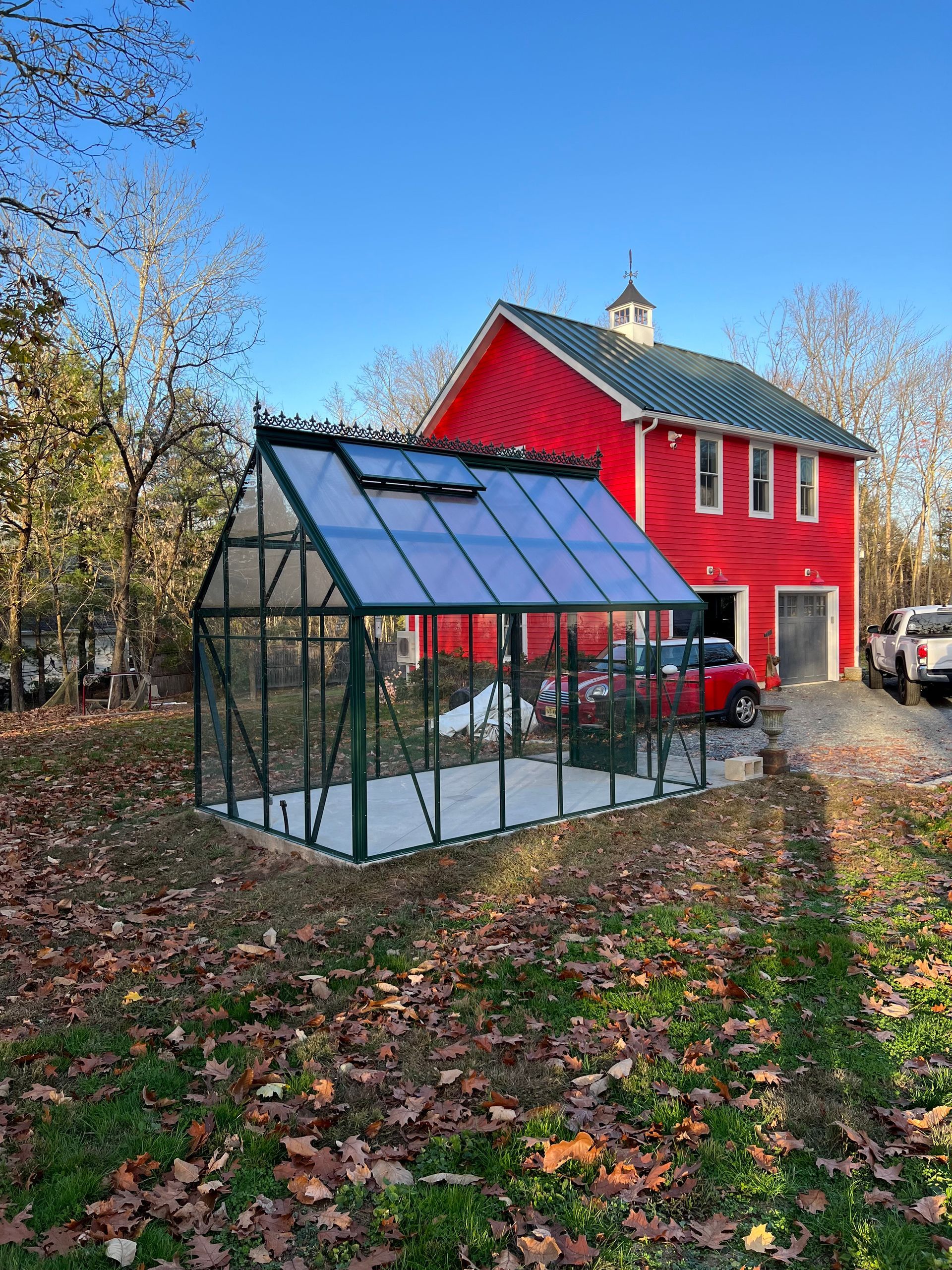 A greenhouse is sitting in front of a red barn.