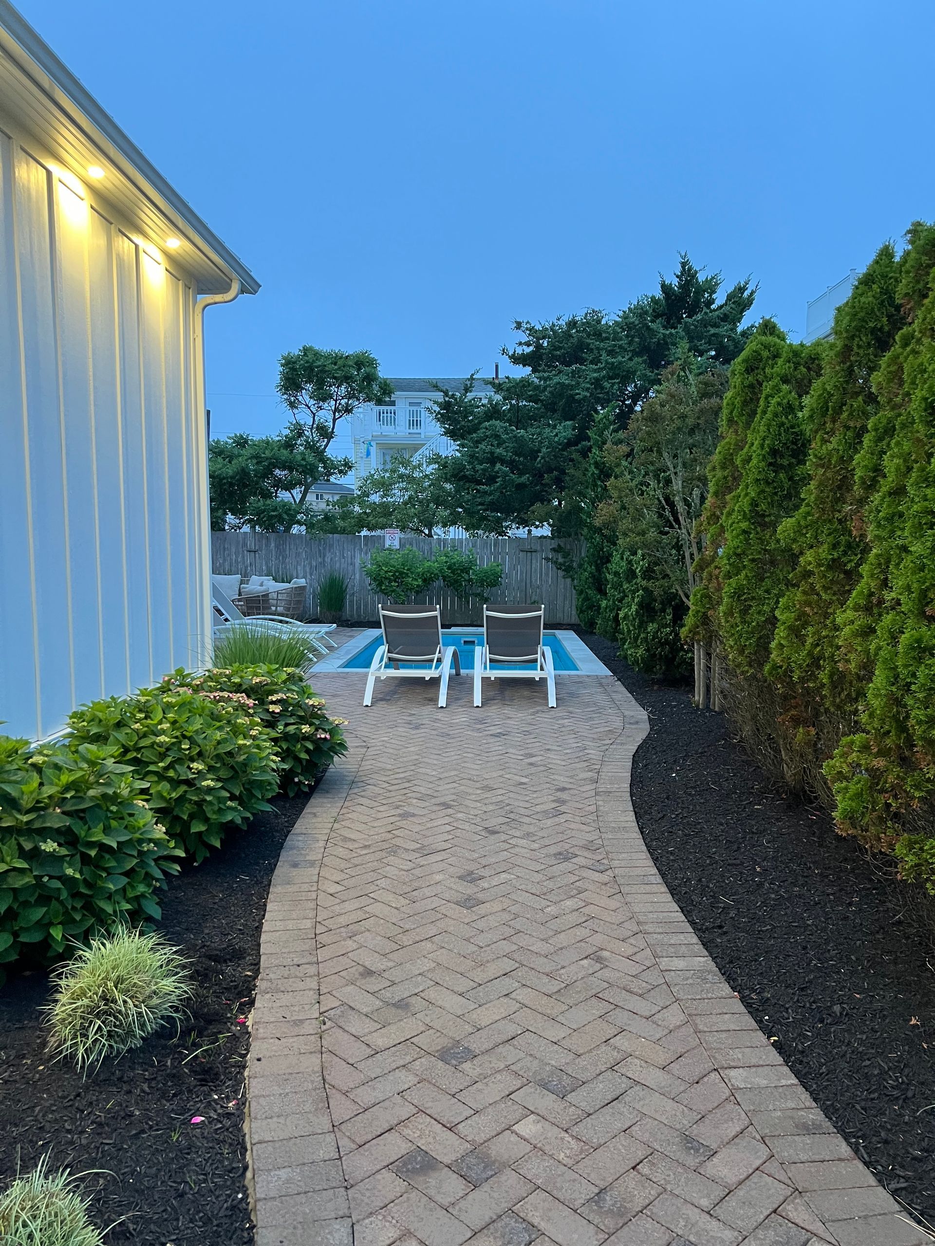 A brick walkway leading to a pool with two chairs on it