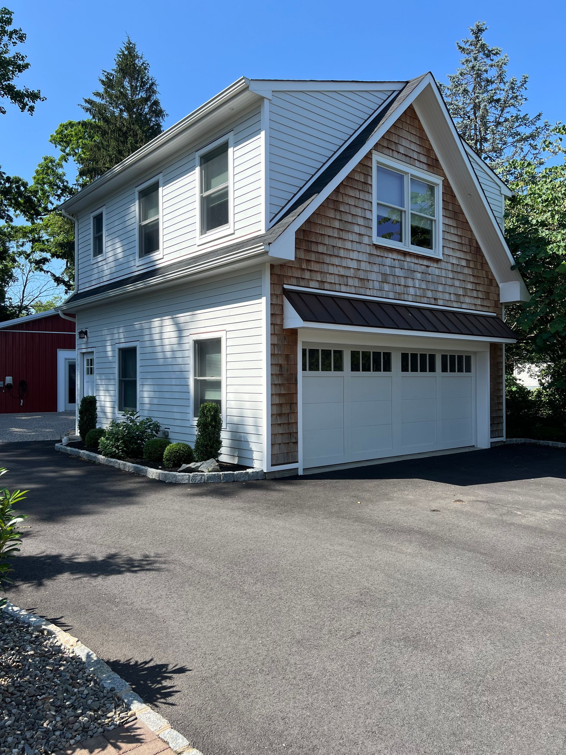 A white house with a garage and a red barn in the background