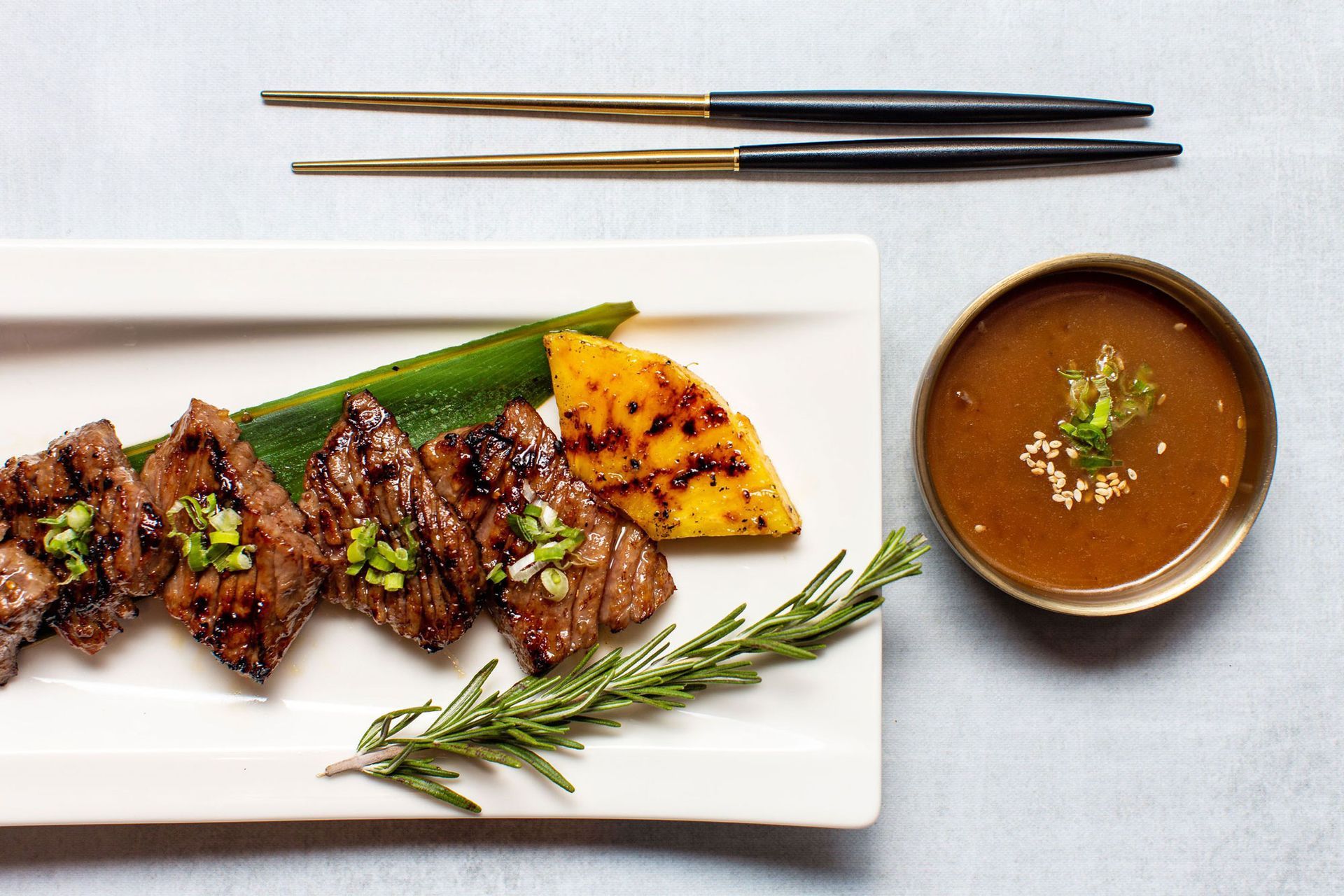 A white plate topped with meat and vegetables next to a bowl of soup and chopsticks.