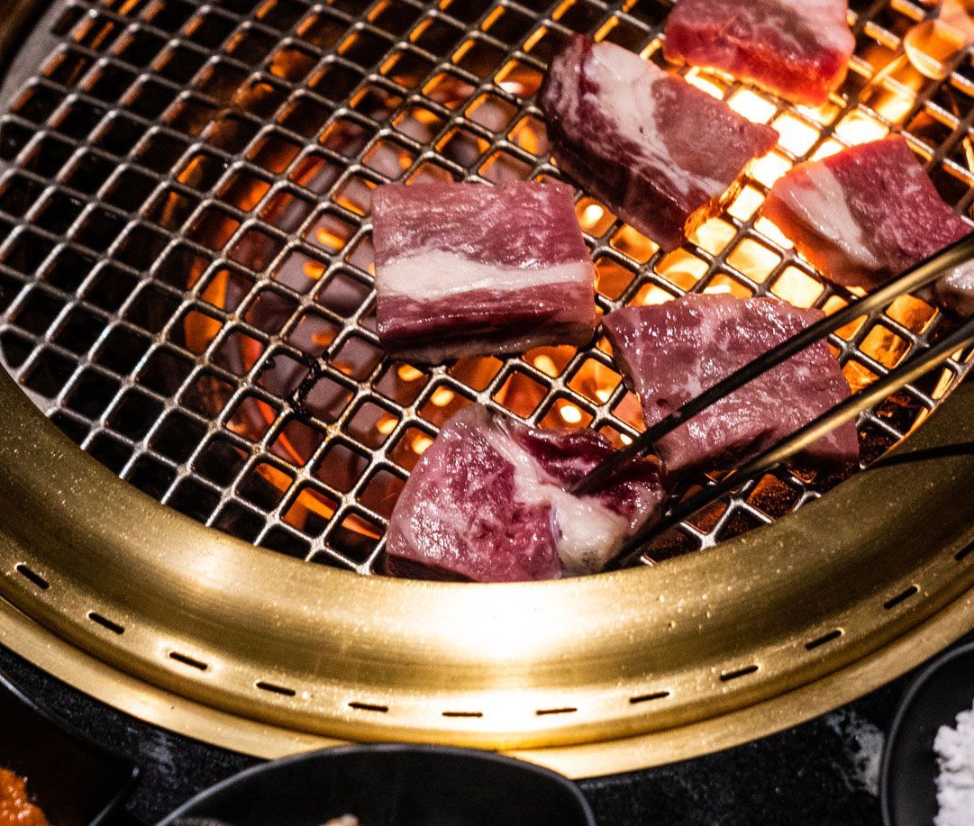 Meat is being cooked on a grill with tongs.