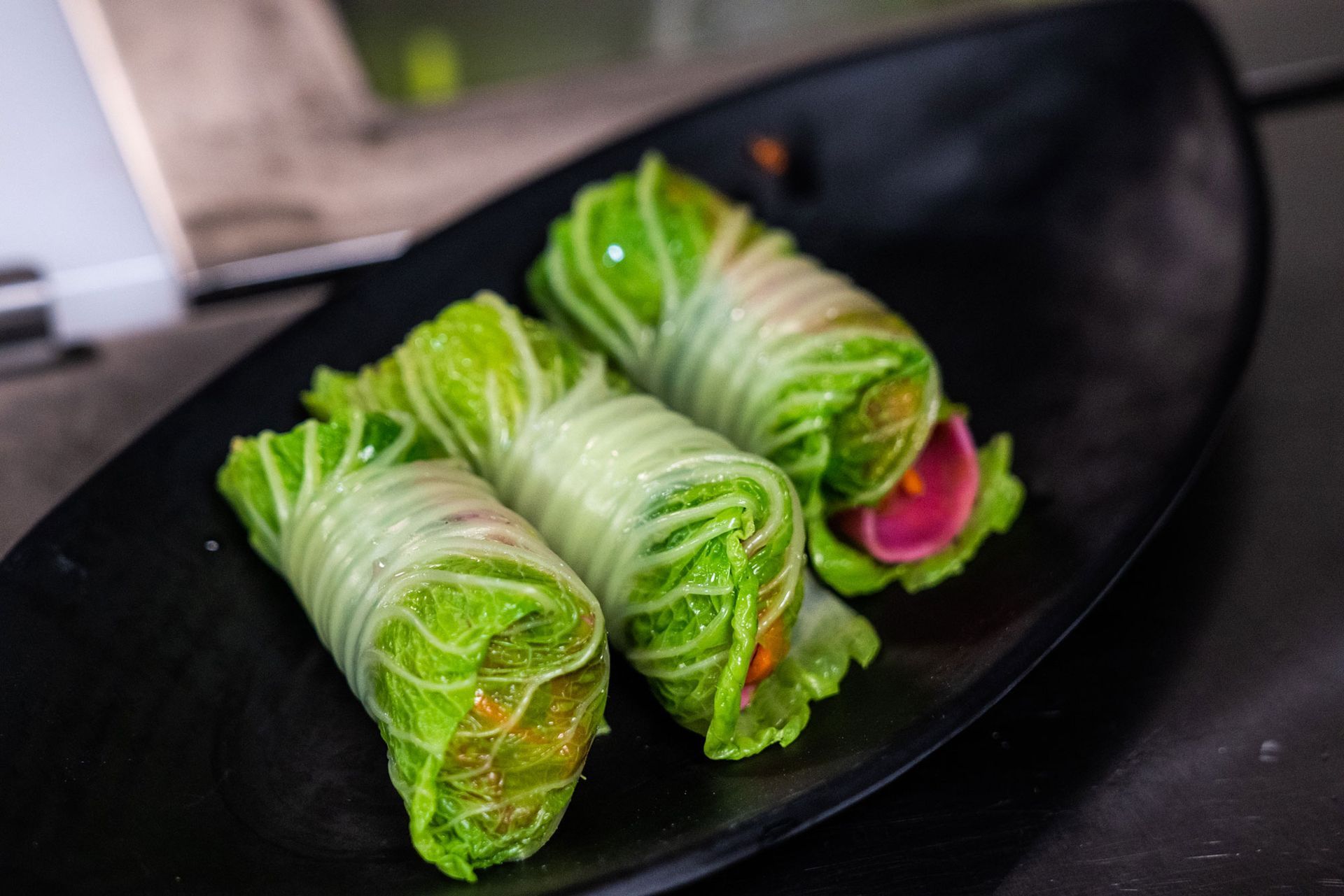A close up of three cabbage rolls on a black plate.