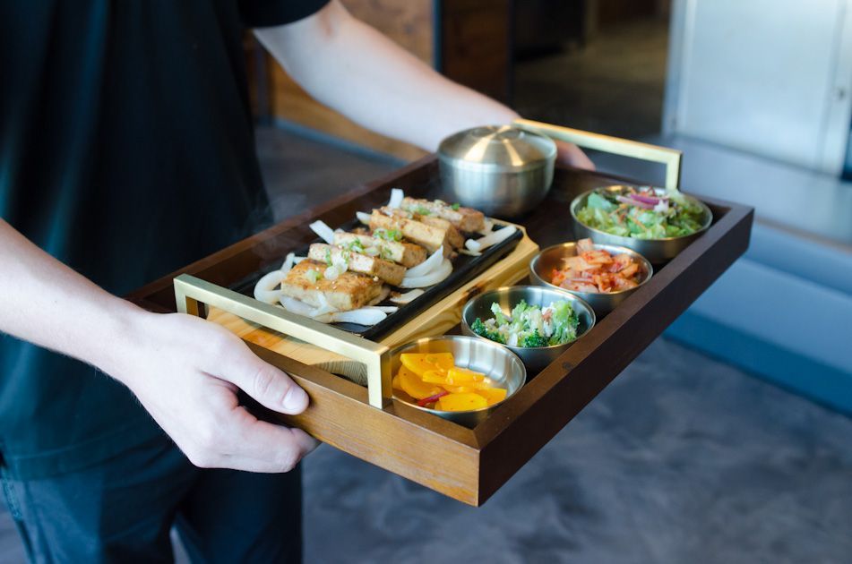 Korean barbecue spread with raw meats, vegetables, and a grill on a dark dining table