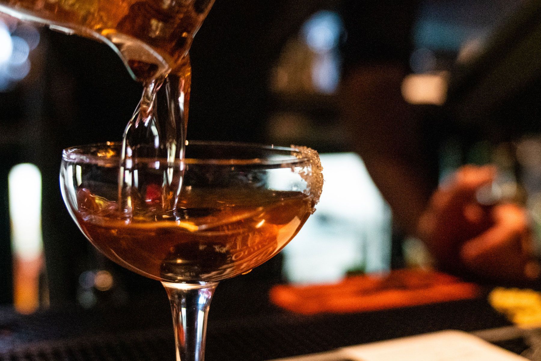 A bartender is pouring a drink into a martini glass
