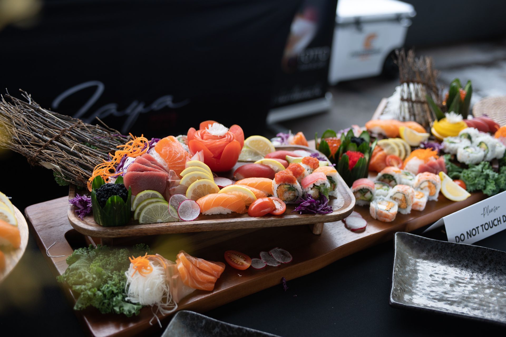 Assorted sushi platters on wooden trays, topped with colorful fish, shrimp, and garnishes on a dark table