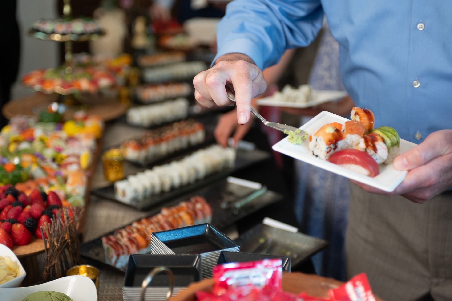 Man serving sushi from a buffet table onto a white plate