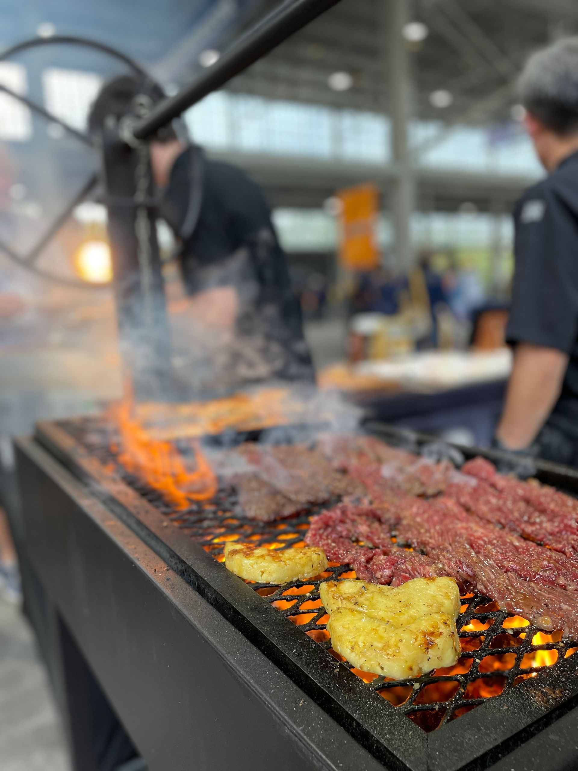 Large grill with smoky flames cooking skewers of meat and vegetables at an outdoor market