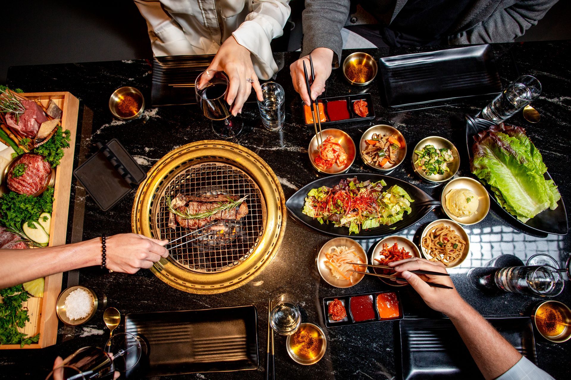 People enjoying Korean BBQ at a table with grilled meat, side dishes, and drinks.