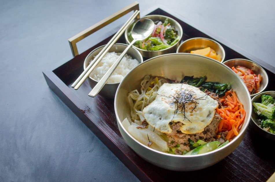 A bowl of food is on a wooden tray with chopsticks.