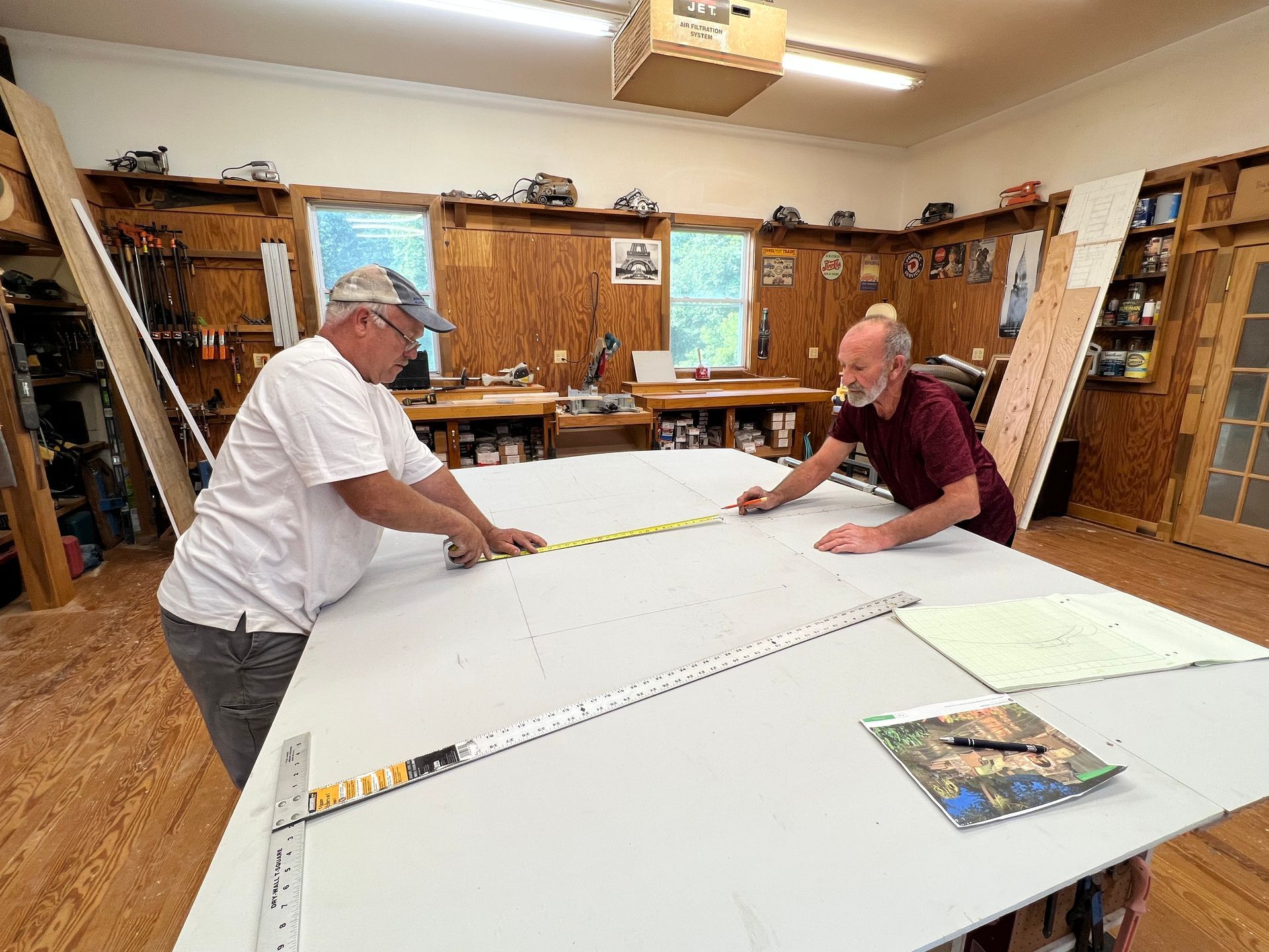 two men are measuring a large piece of wood in a workshop .