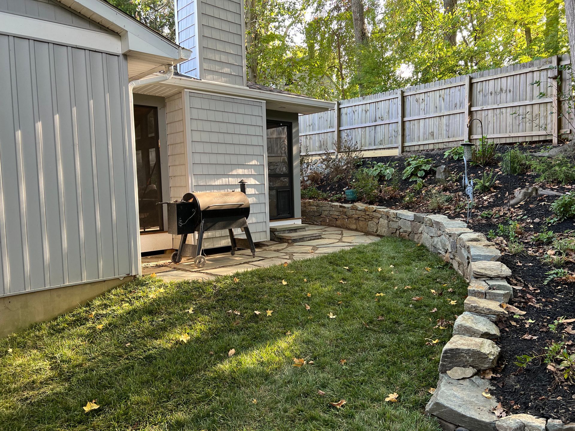 a backyard with a fence, a stone wall, and a grill.