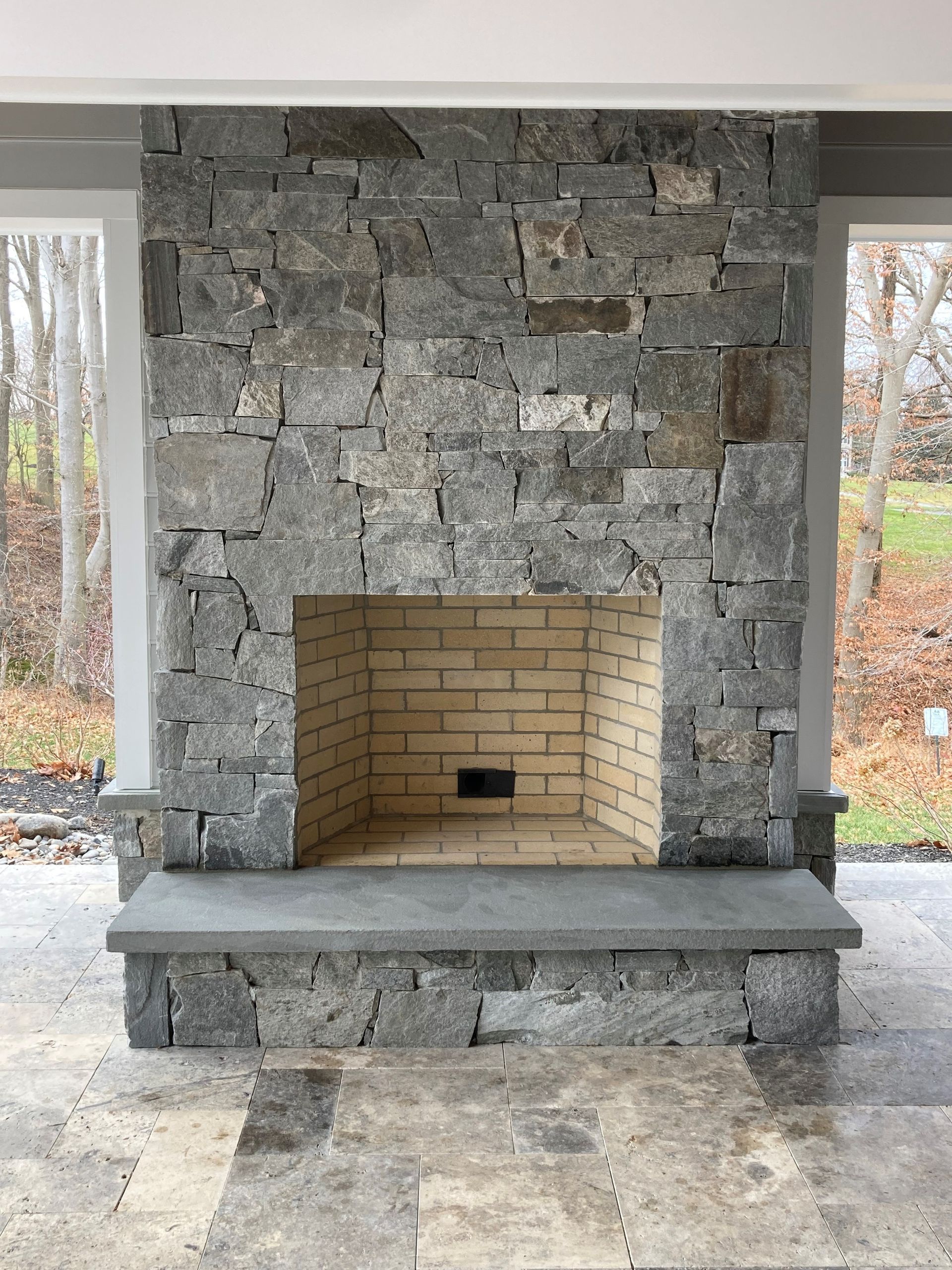a stone fireplace with a brick hearth is sitting under a covered patio .