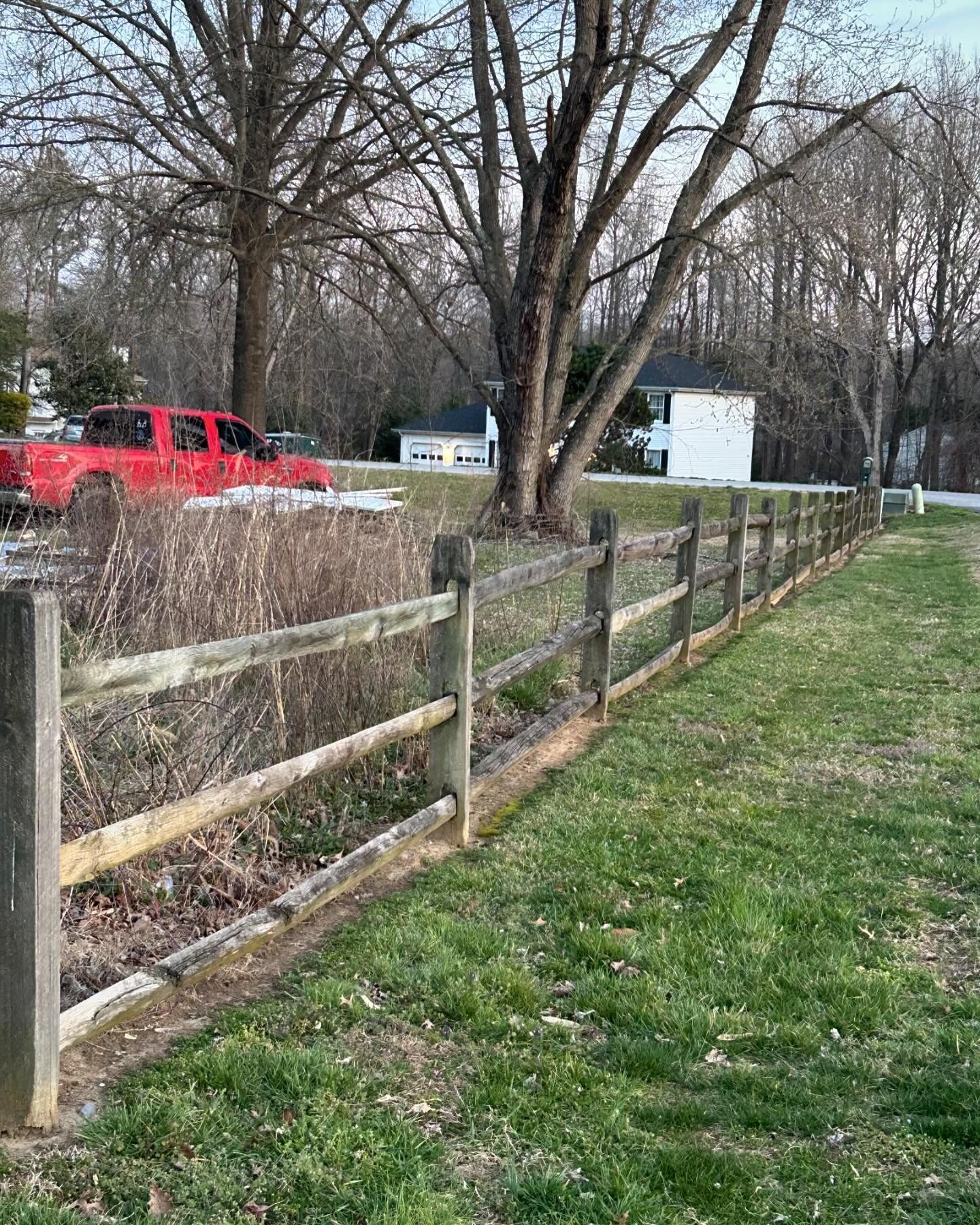 A wooden fence surrounds a grassy field with a red truck parked in the background