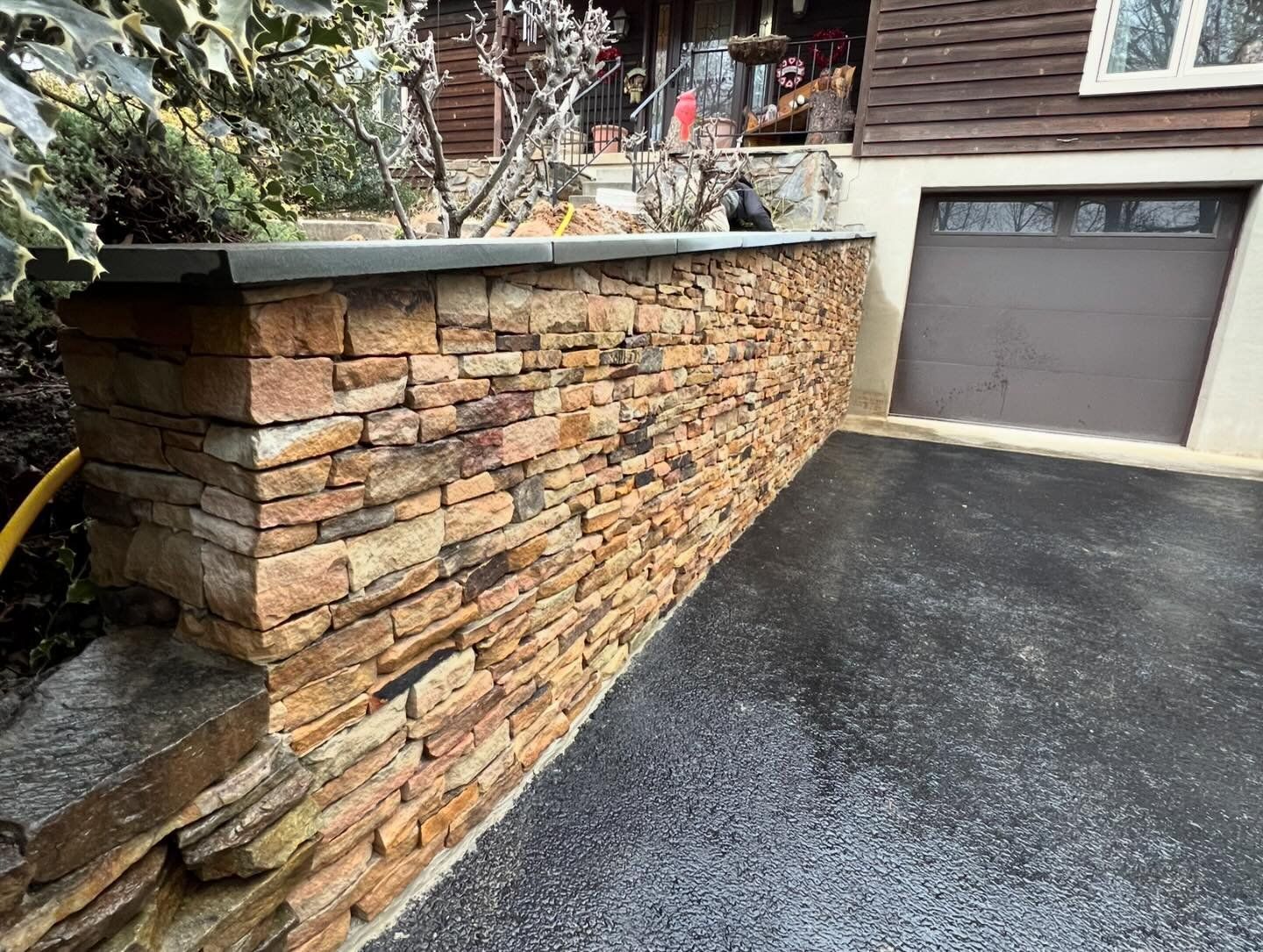A stone wall is sitting next to a garage door in front of a house