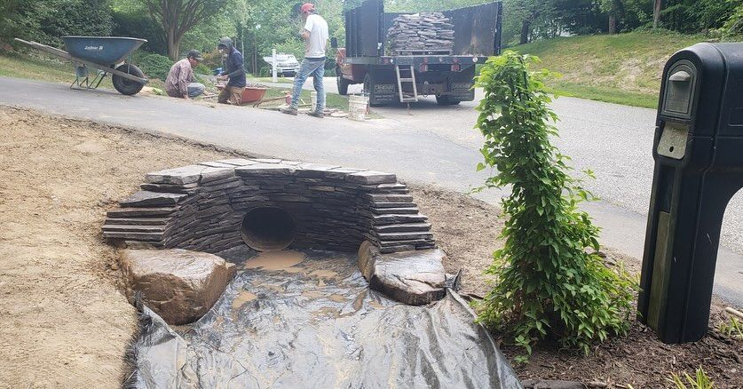A group of people are working on a stone wall in front of a mailbox