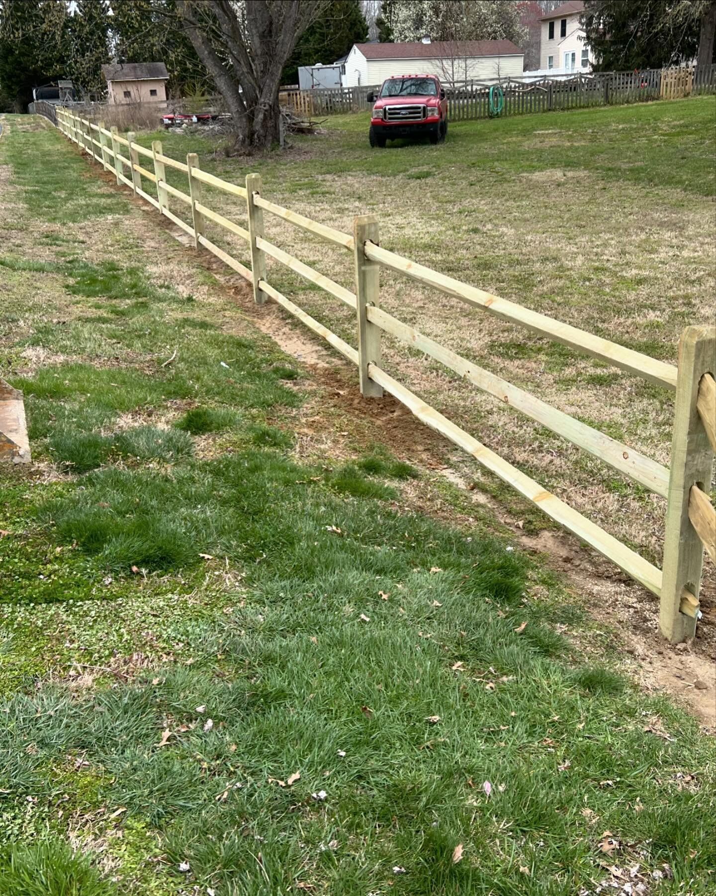 A wooden fence surrounds a grassy field with a red truck parked in the background