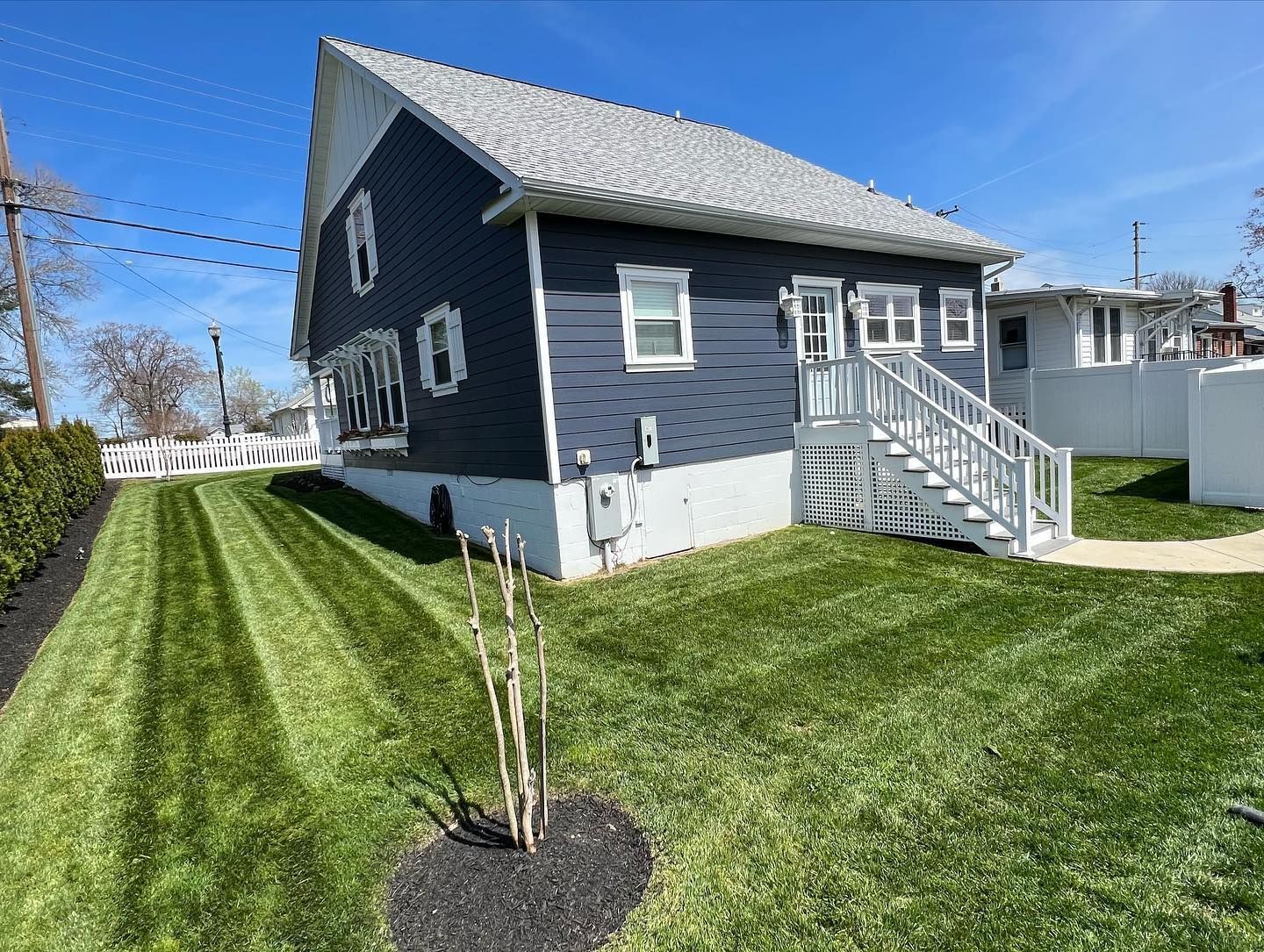 a gray-blue and white house with stairs and a lush green lawn in front of it .