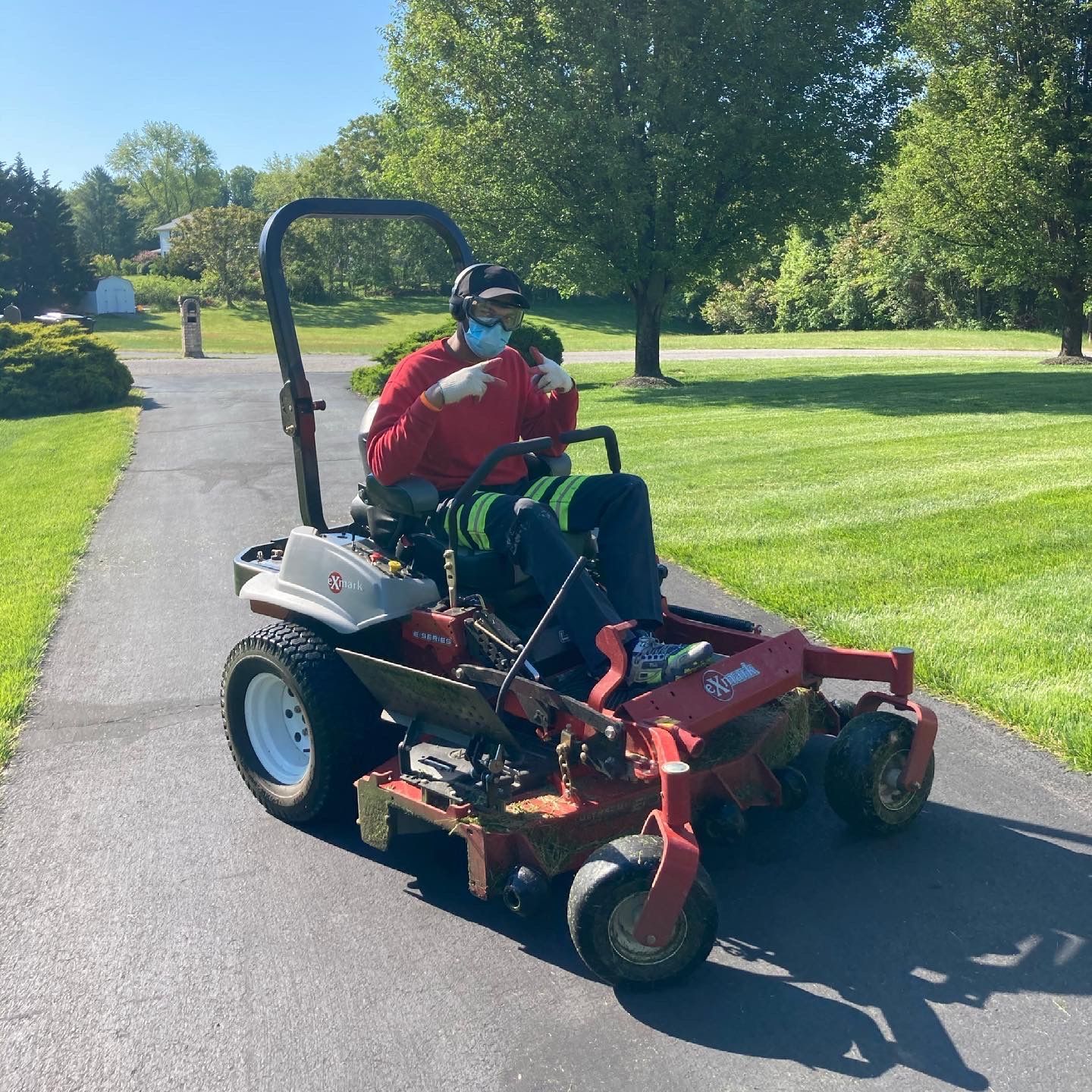 a man wearing a mask is riding a lawn mower down a driveway .