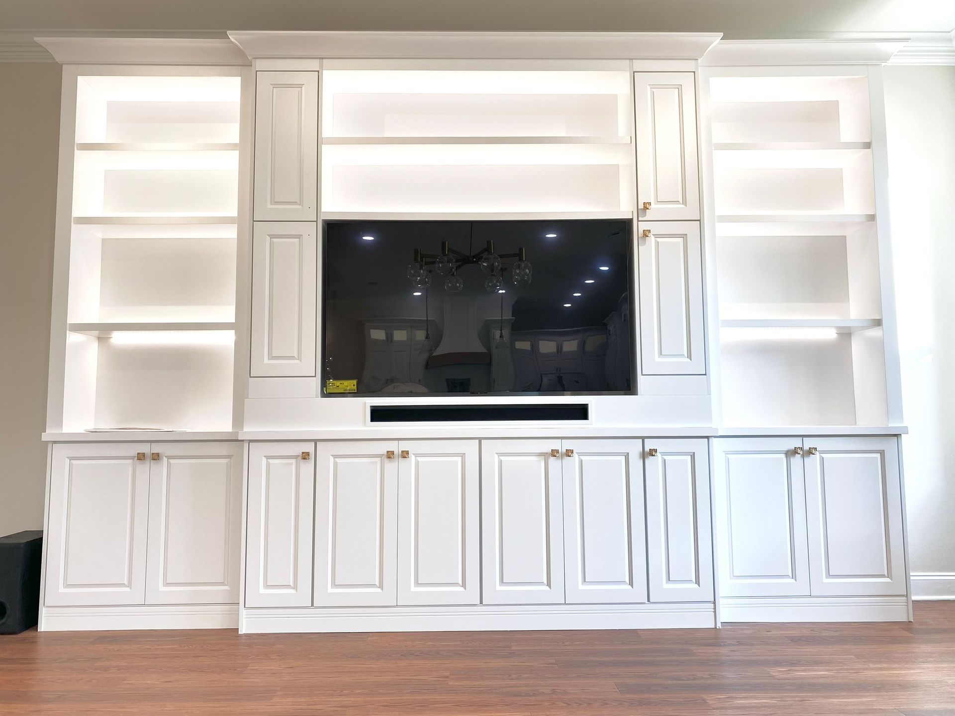 White built-in entertainment center with a large TV, shelving, and cabinets against a light-colored wall.