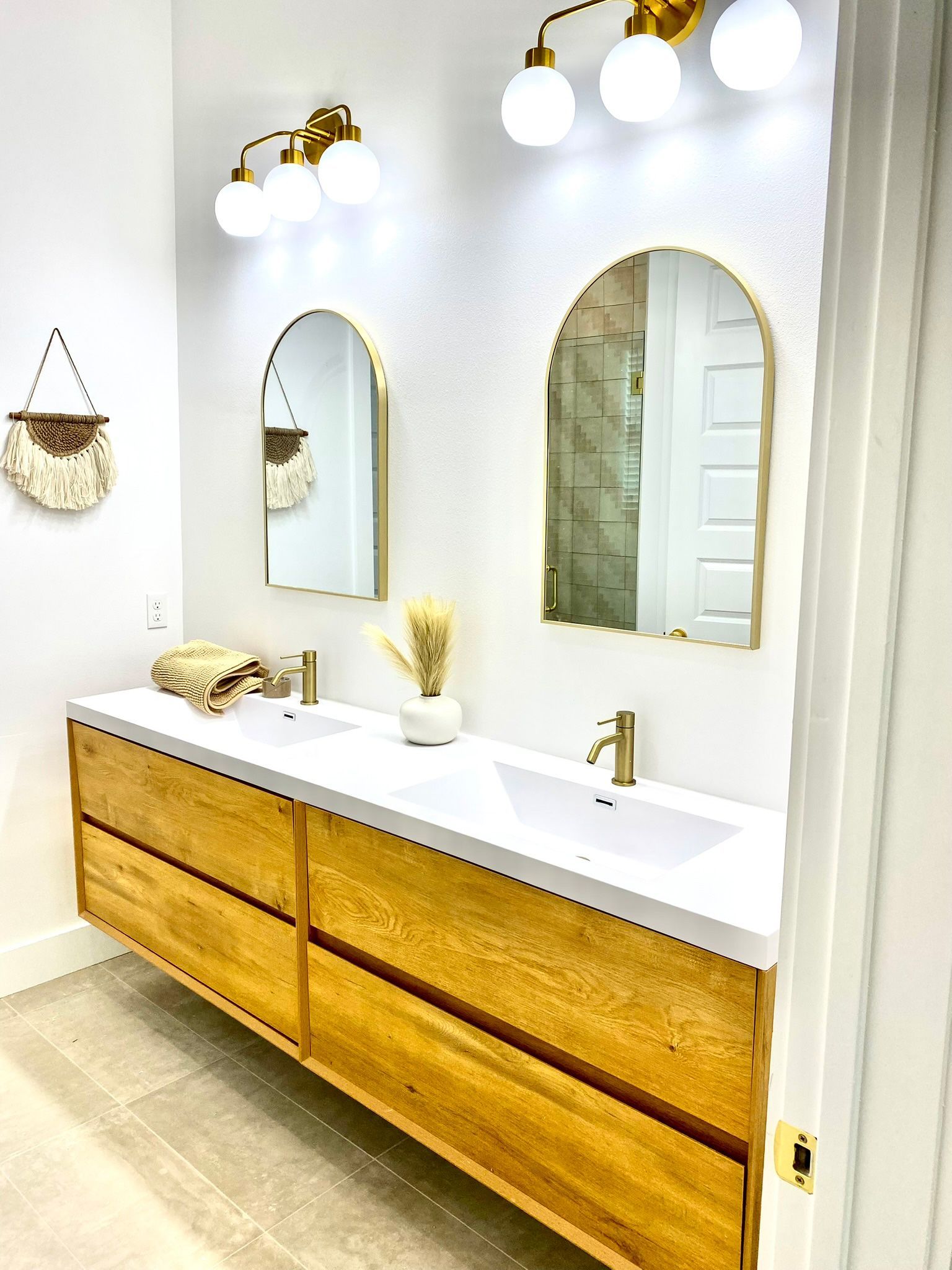 Bathroom with wood vanity, arched gold mirrors, and gold fixtures.
