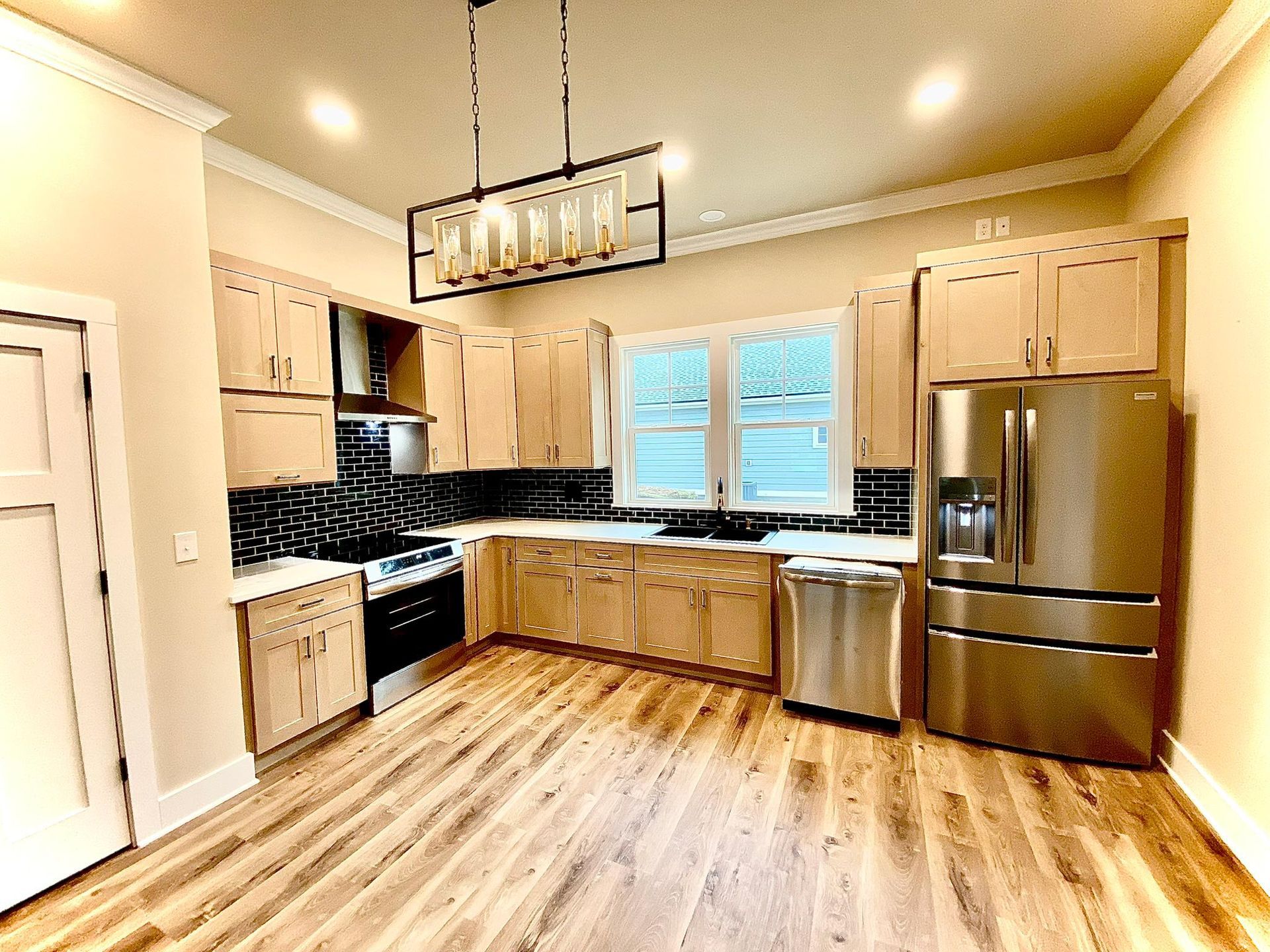 Kitchen with light wood cabinets, stainless steel appliances, and black tile backsplash.