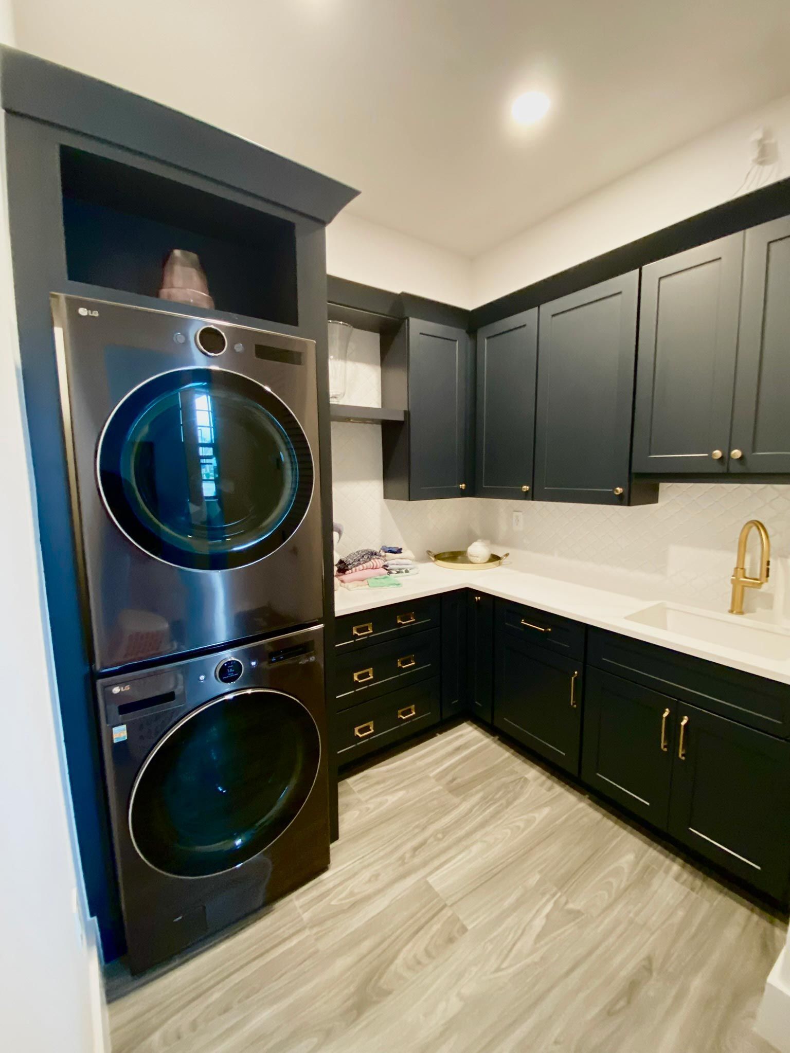 Stacked washer and dryer in a laundry room with dark cabinets, a white countertop, and light wood-look flooring.