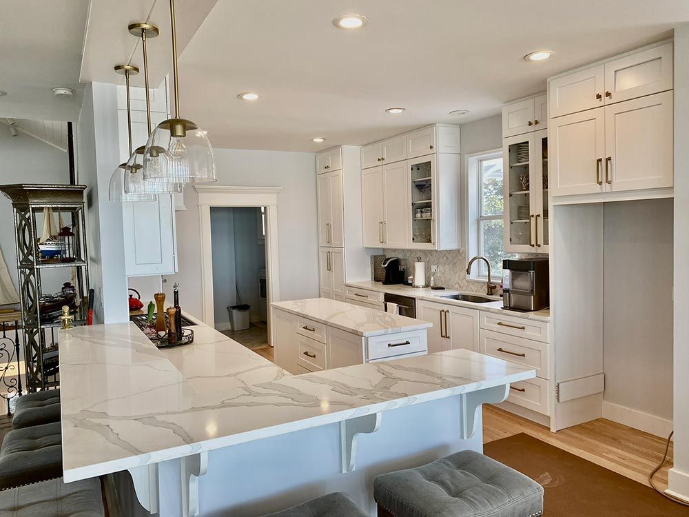 White kitchen with quartz countertops and an island, featuring cabinets, a sink, and pendant lights.