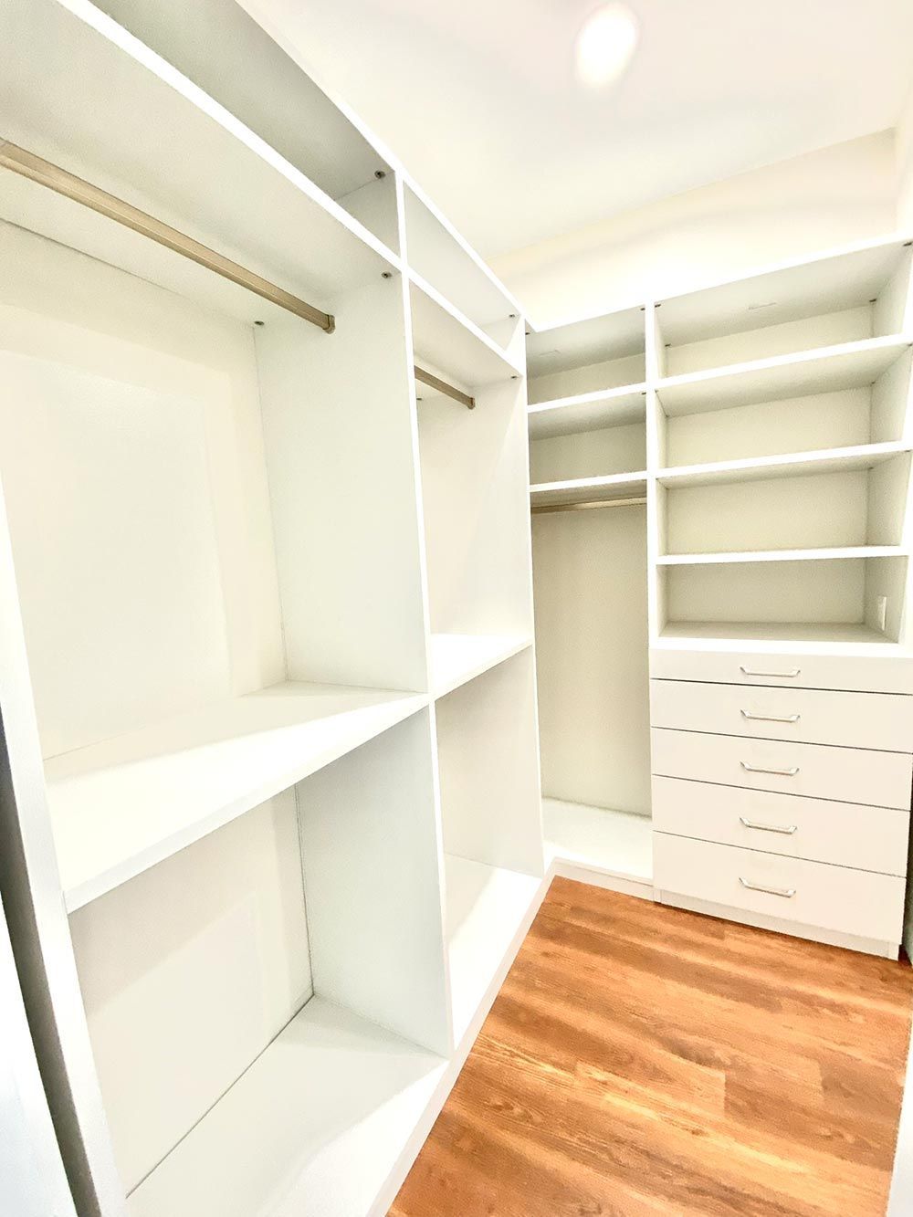 White walk-in closet with shelves, hanging rods, and a set of drawers; wood floor.