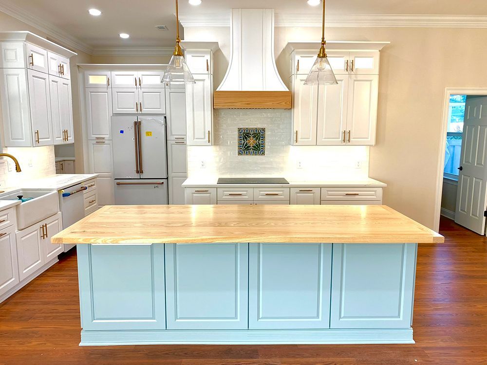 Light blue kitchen island with light wood countertop, white cabinets, and wooden range hood.