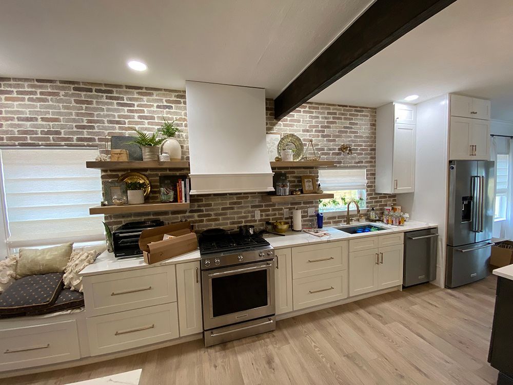 A kitchen with white cabinets , stainless steel appliances , and a brick wall.